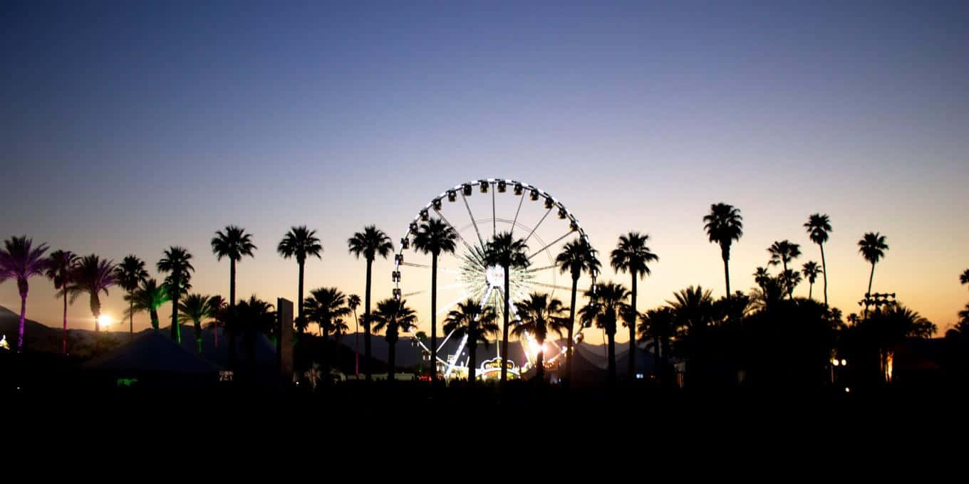 Coachella 桌布 壁紙 — 剪影棕櫚樹襯托著發光的摩天輪，背景是帶有溫暖橙色和冷藍色漸變的暮色天空。
