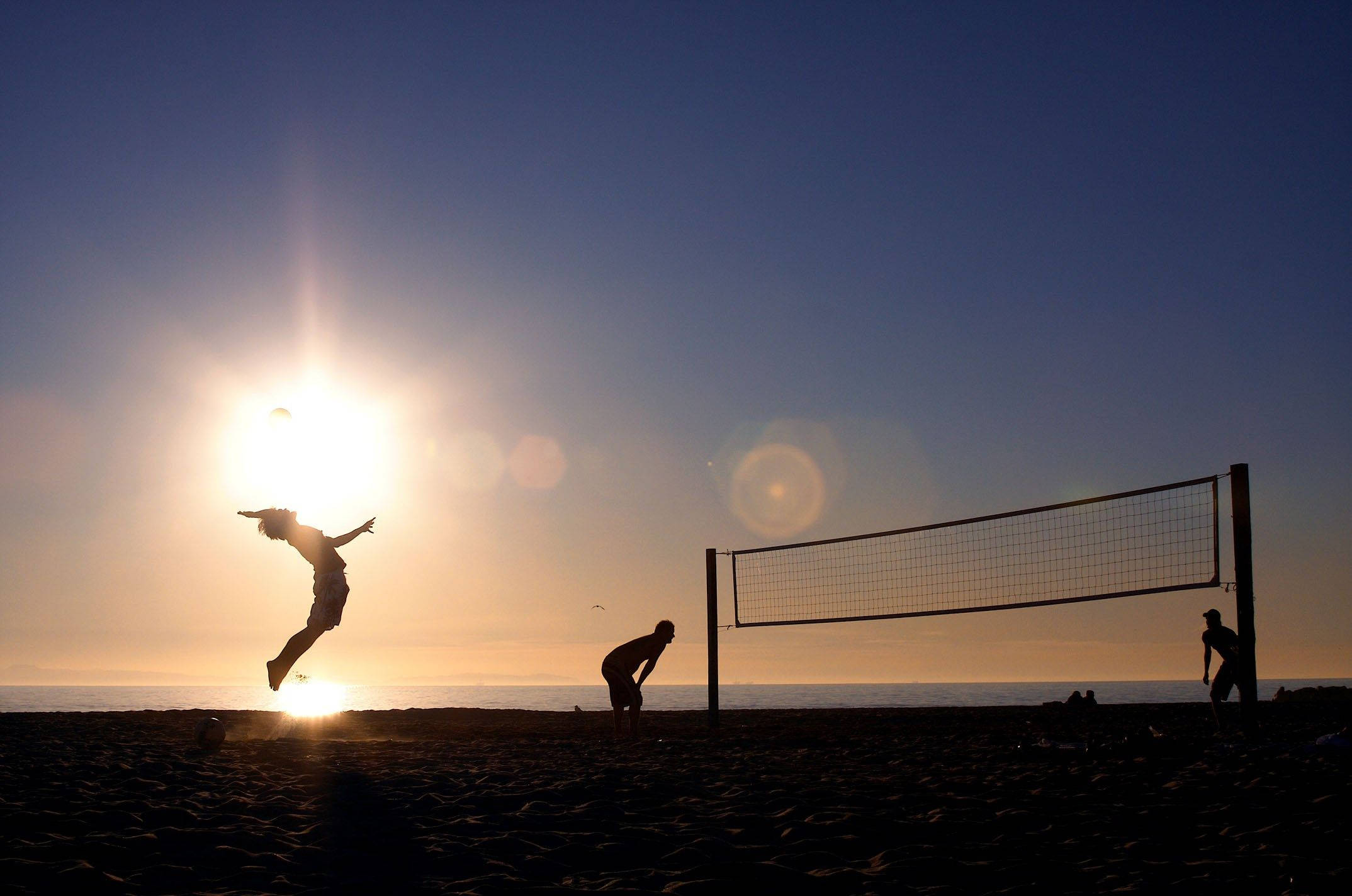 Volleyball 桌布 壁紙 — 剪影沙灘排球運動員在海洋上輝煌的日落中跳躍和潛水。