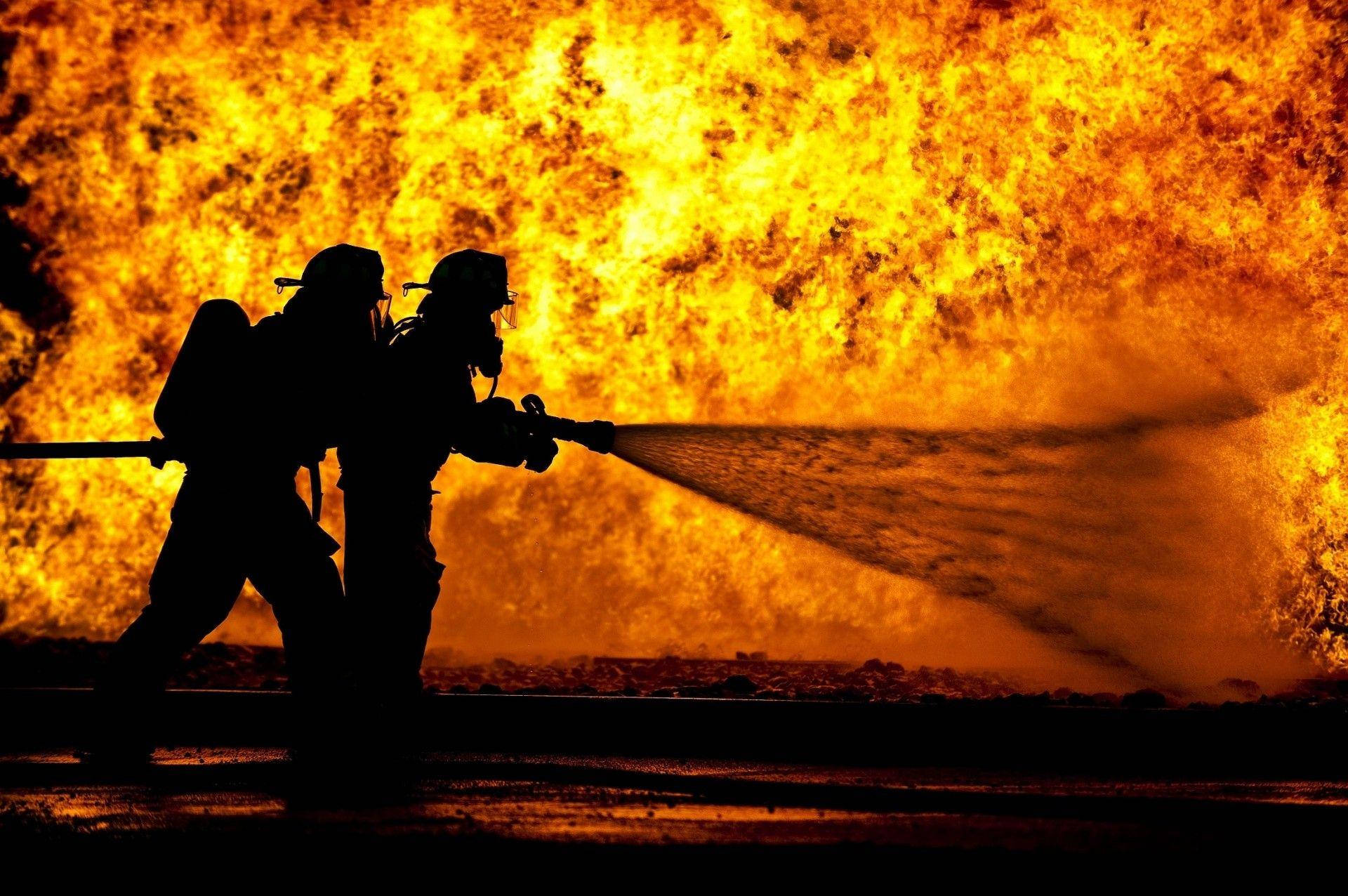 Firefighter 桌布 壁紙 — 剪影消防員在熾熱的橙色背景下用強勁的水流與咆哮的烈火搏鬥。