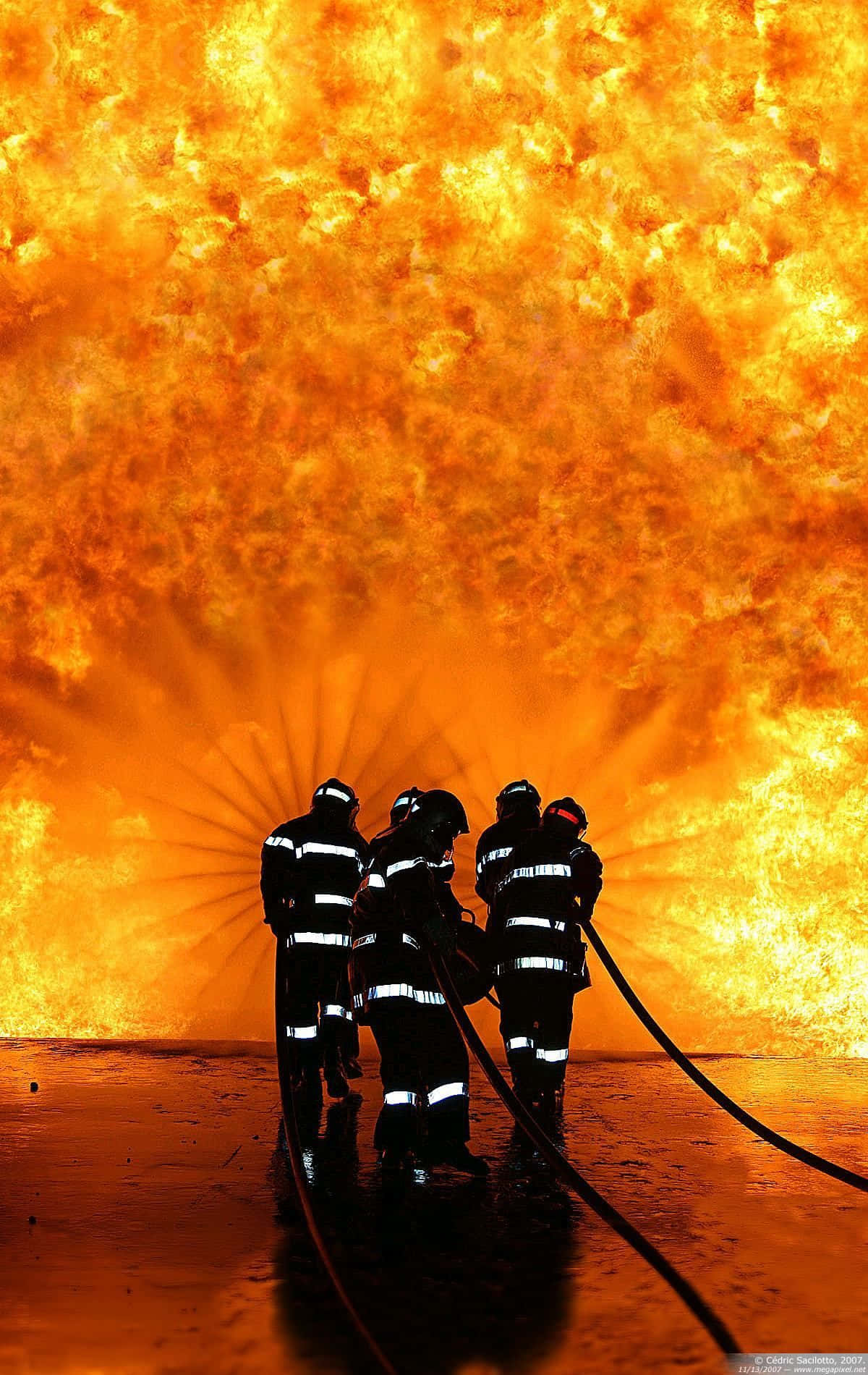 Fire Department 桌布 壁紙 — 剪影消防員用消防喉對抗高聳的火災，背景是熾熱的橙色。