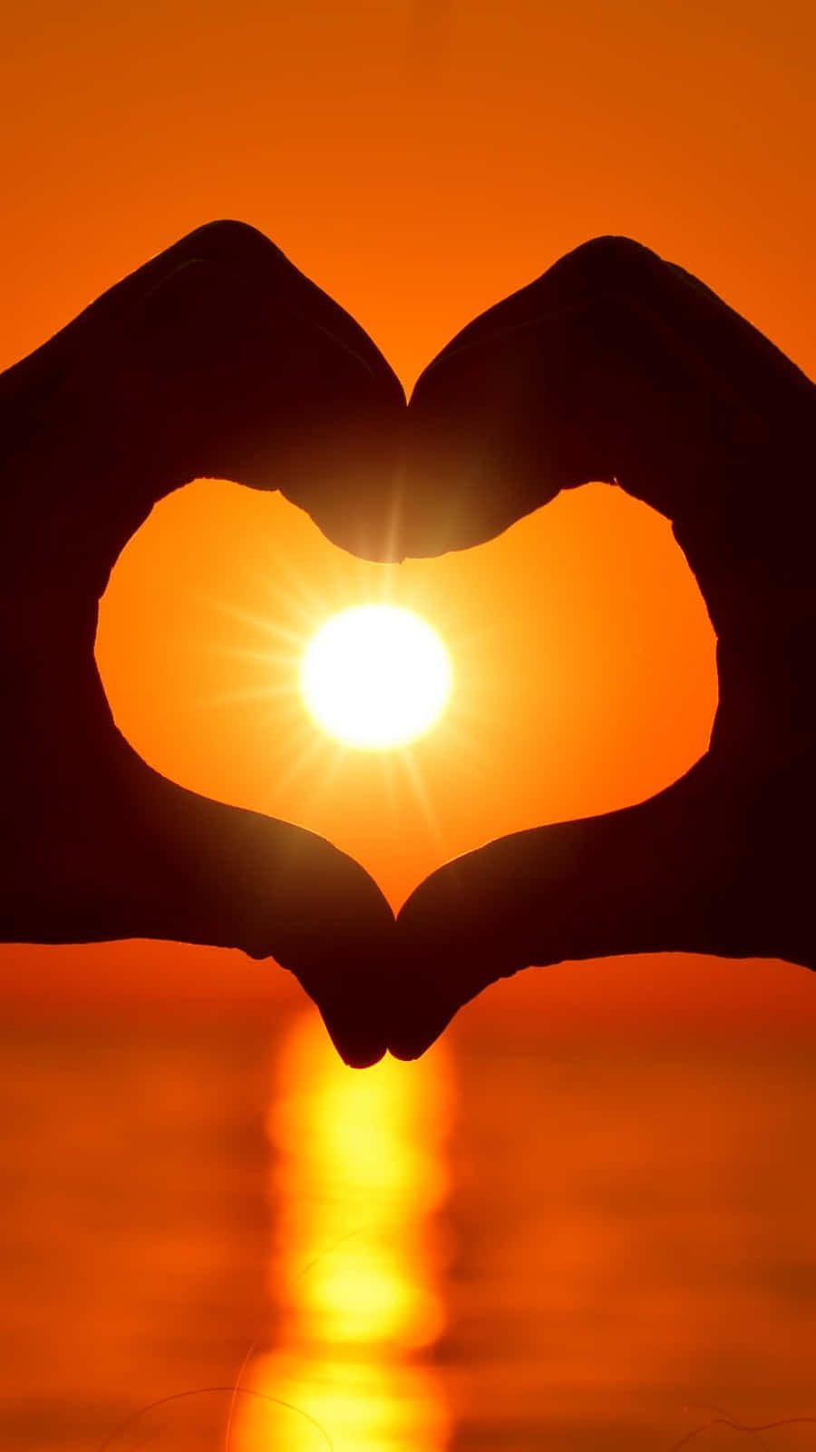 Orange Heart 桌布 壁紙 — 剪影的手形成心形，框住日落時平靜水面上發光的太陽。