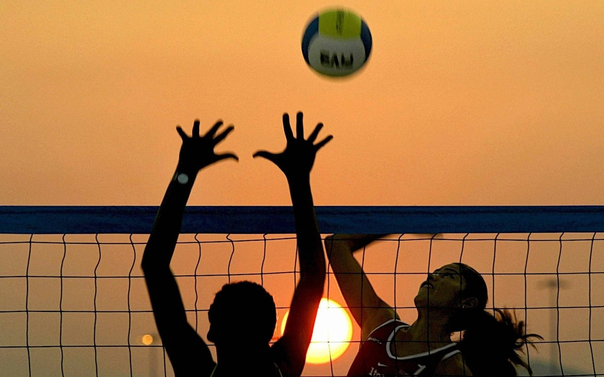 Volleyball 桌布 壁紙 — 剪影的排球運動員跳起扣球，背景是發光的日落天空。
