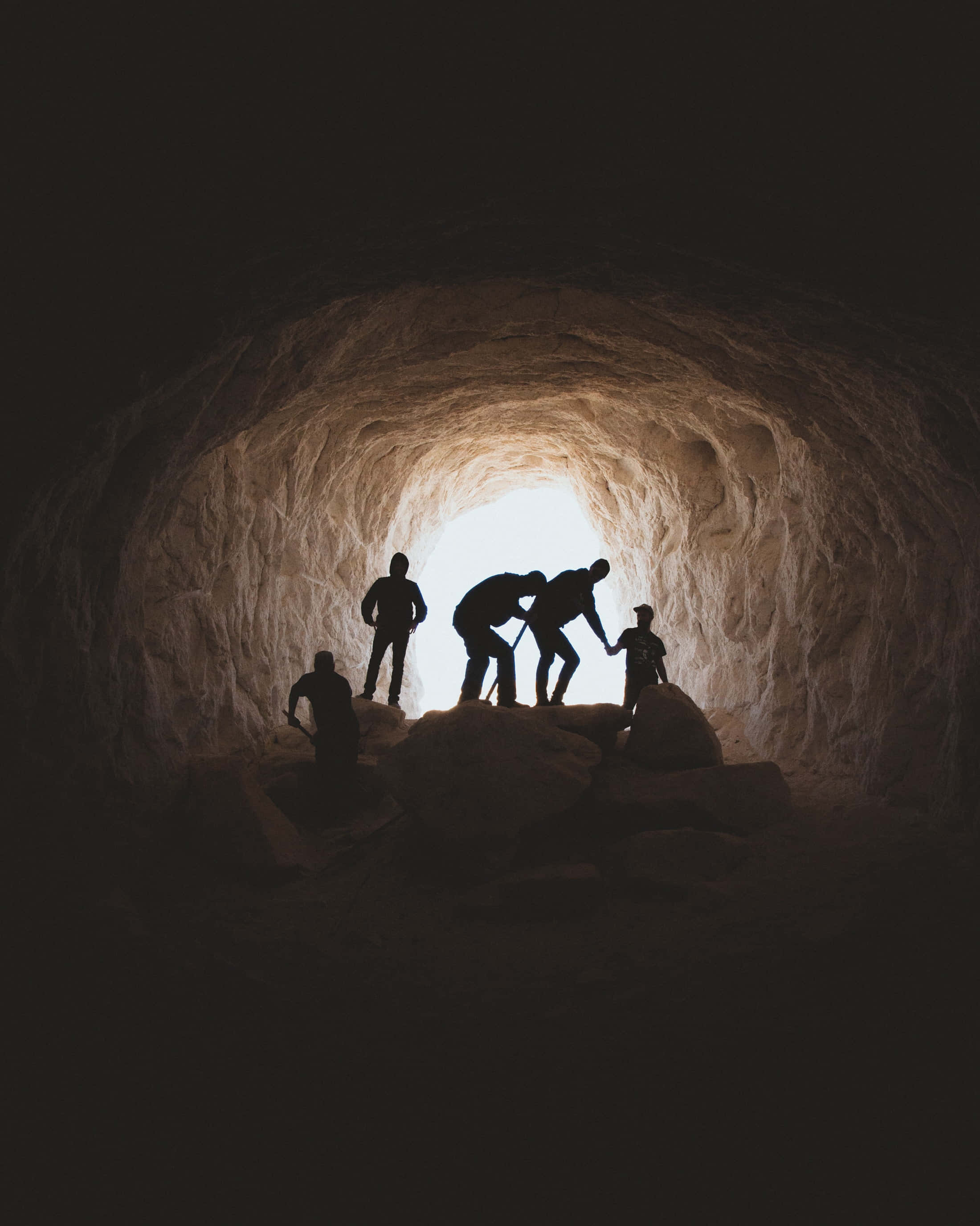 Cave 桌布 壁紙 — 剪影的攀岩者在前方明亮日光照射的黑暗洞穴口攀爬岩石地形。