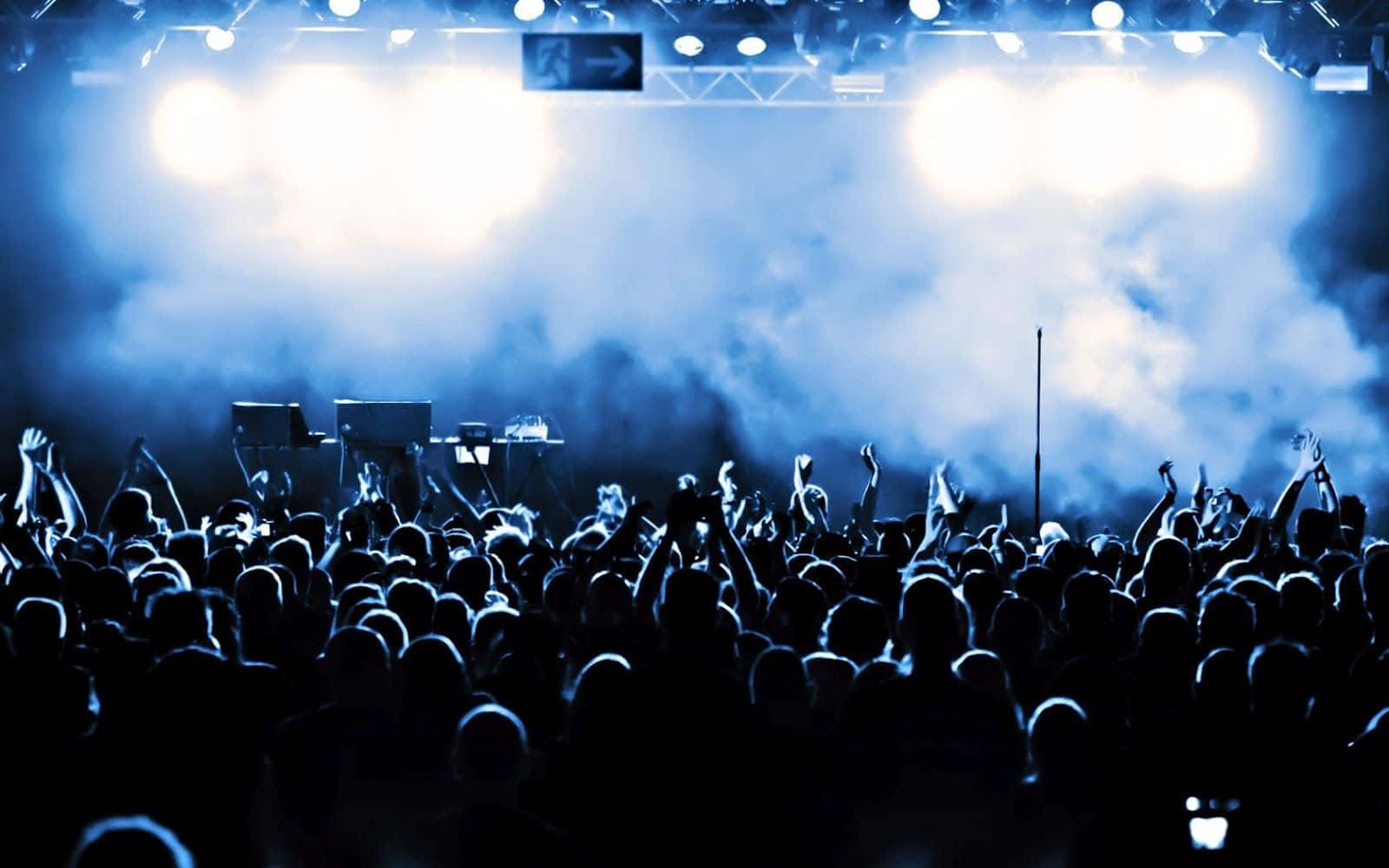 concert 桌布 壁紙 — 剪影的演唱會人群在明亮的藍色舞台燈光和旋轉煙霧下舉起雙手。