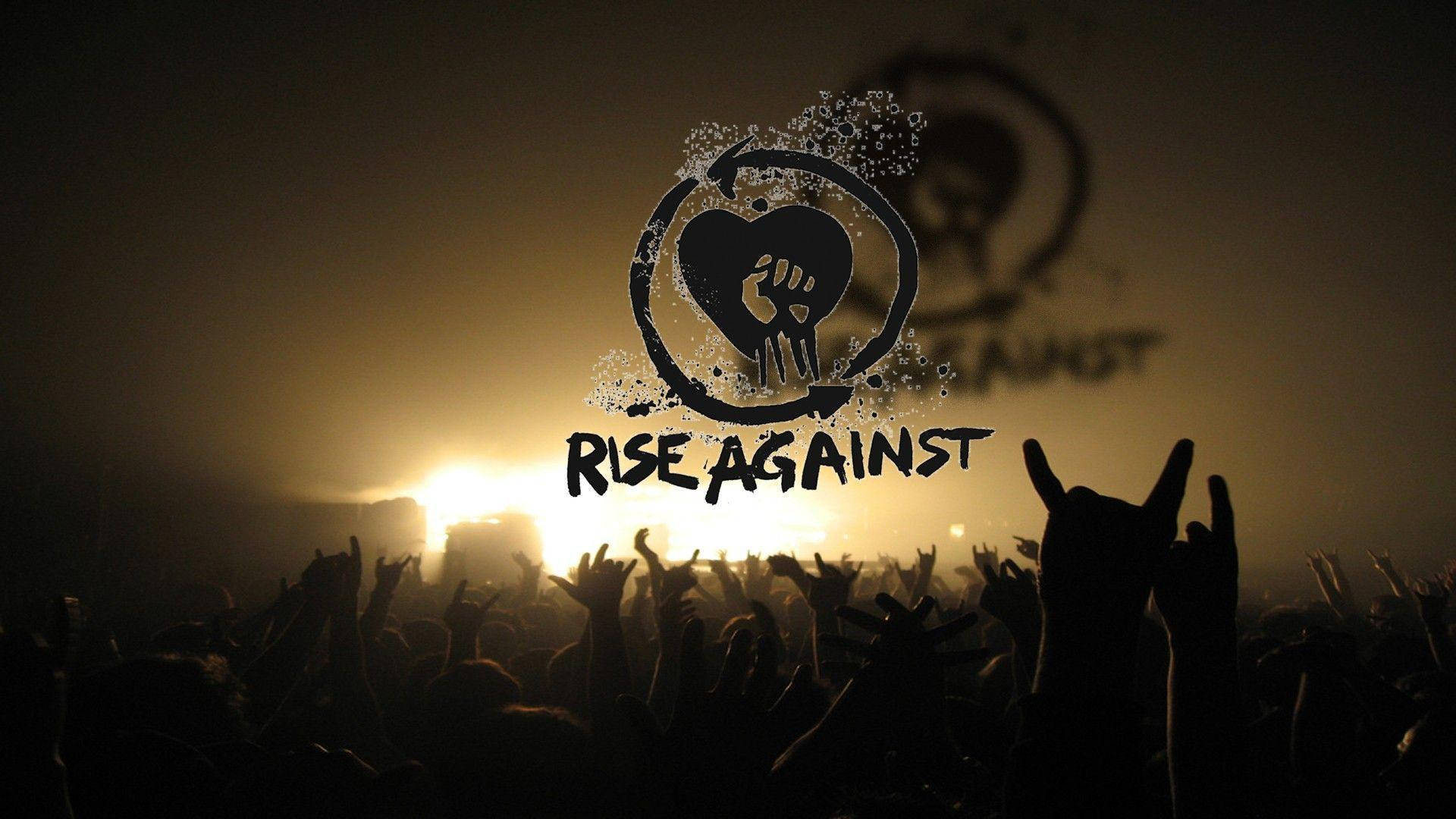 Rock 桌布 壁紙 — 剪影的演唱會人群在溫暖的舞台燈光下舉起雙手，'Rise Against' 標誌在煙霧中發光。