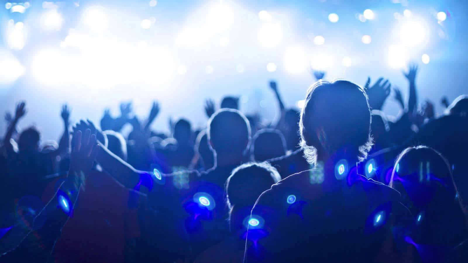concert 桌布 壁紙 — 剪影的演唱會人群高舉雙手，沐浴在明亮的藍色舞台燈光和發光手環中。