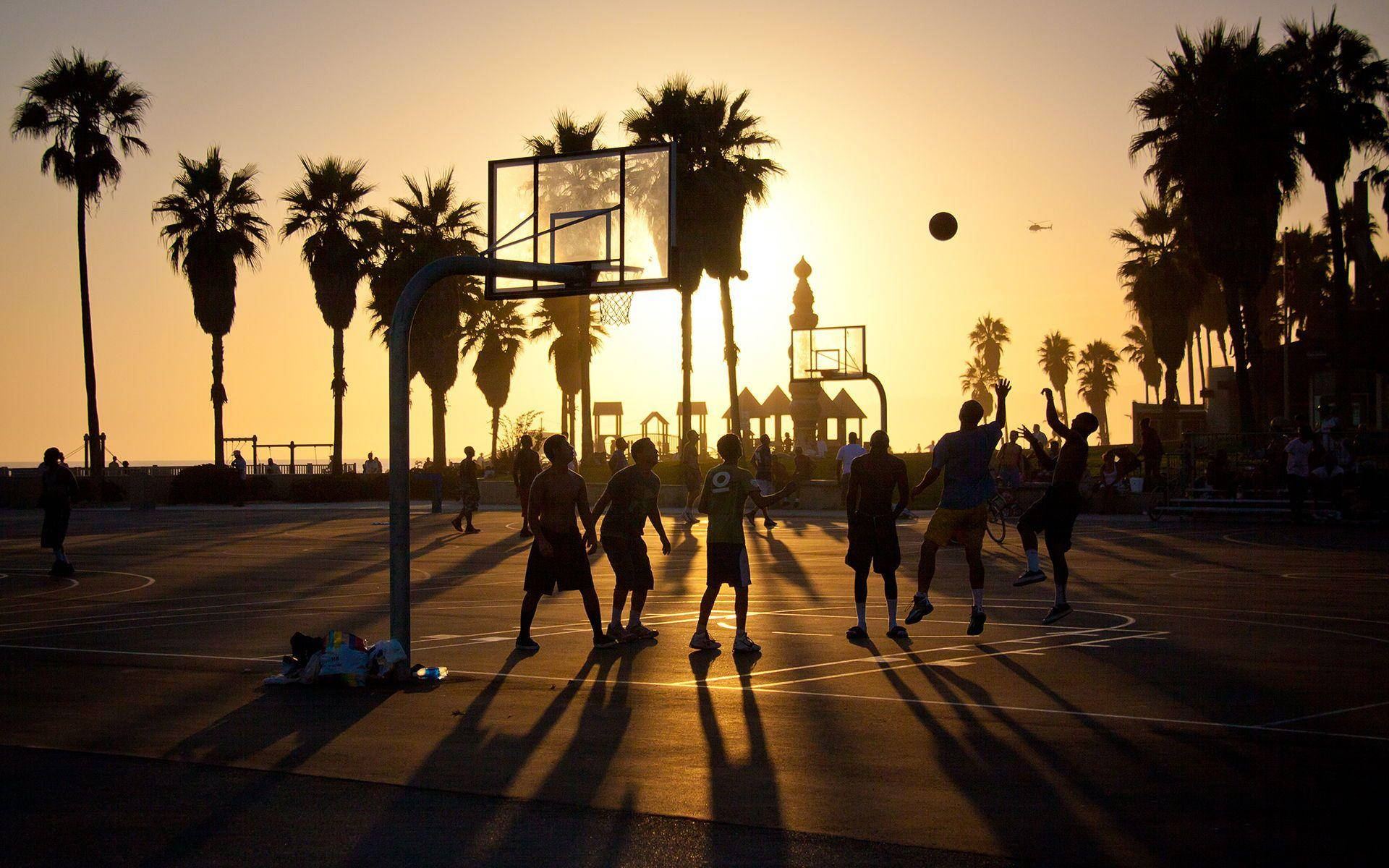 Venice Beach 桌布 壁紙 — 剪影的籃球運動員在戶外球場跳躍和運球，太陽在棕櫚樹後落下，投下長長的影子。