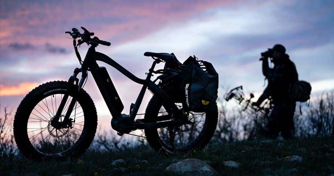 Electric Bike 桌布 壁紙 — 剪影的胖胎單車和攝影師，背景是充滿活力的暮色天空，帶有柔和的雲朵和草地前景。