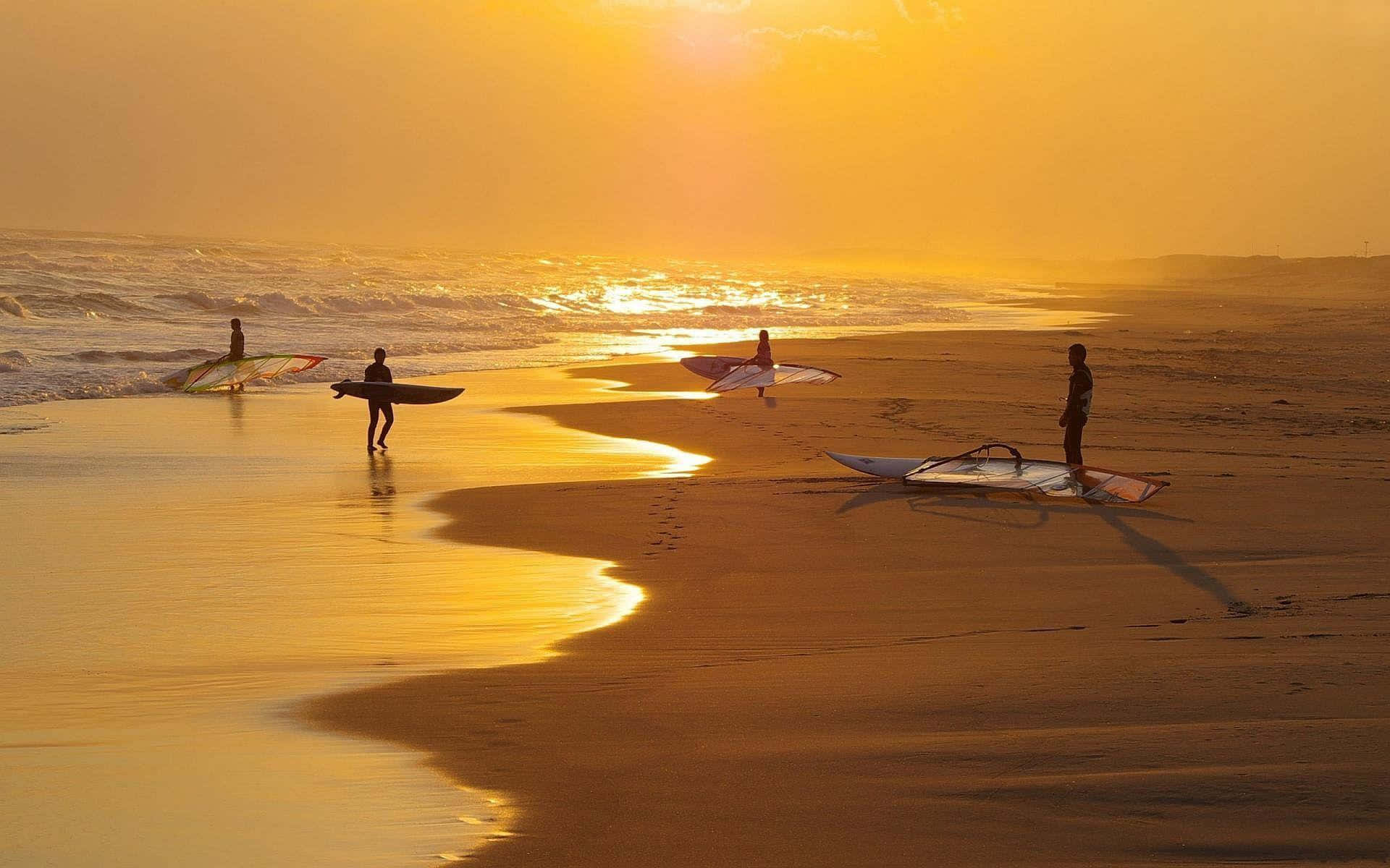 海灘 桌布 壁紙 — 剪影的衝浪者帶著衝浪板在金色沙灘上漫步，夕陽西下，海浪輕輕拍打。