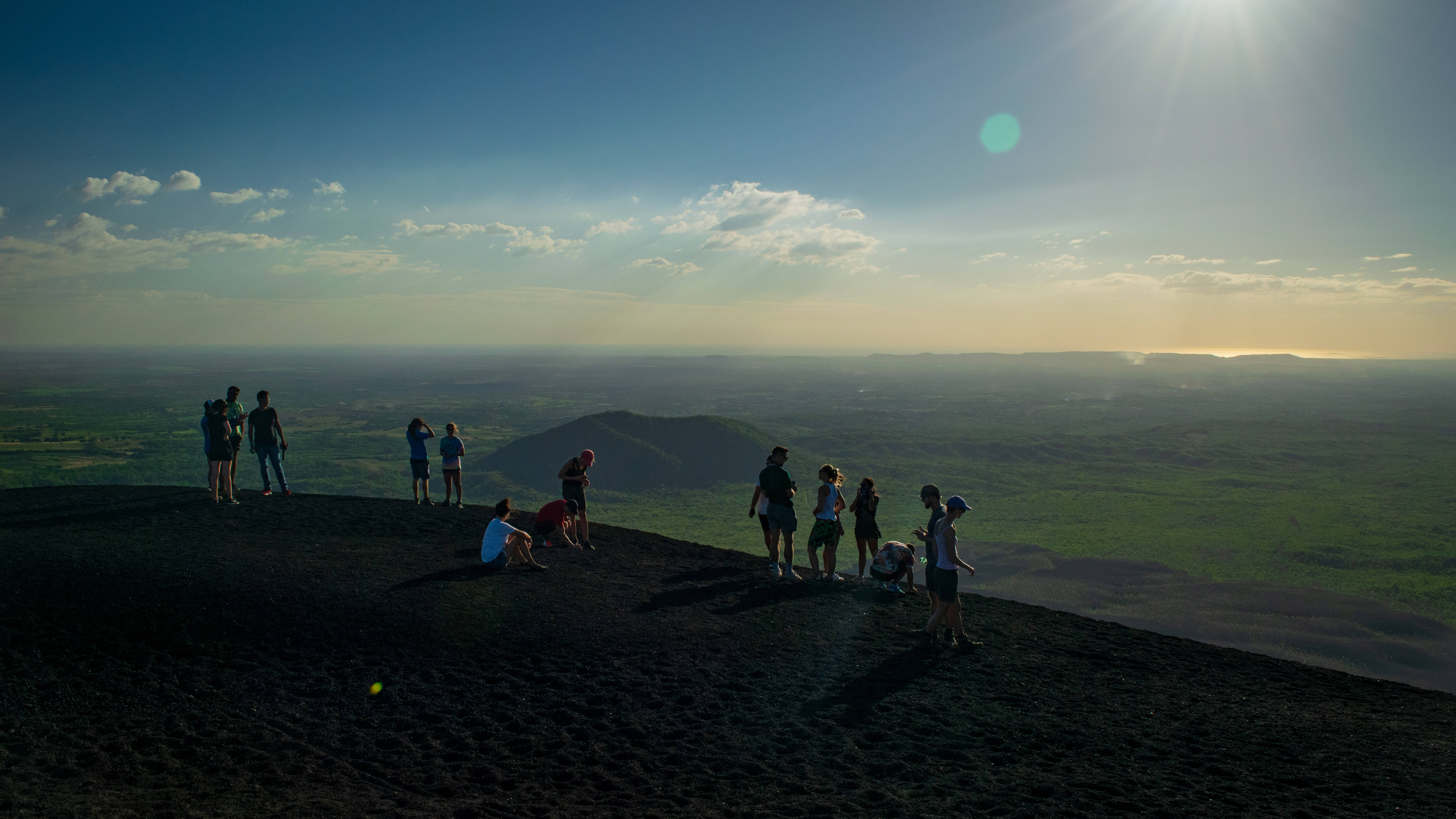 Nicaragua 桌布 壁紙 — 剪影的遠足者站在火山山脊上，沐浴在金色夕陽的光芒中，俯瞰廣闊的綠色山谷。