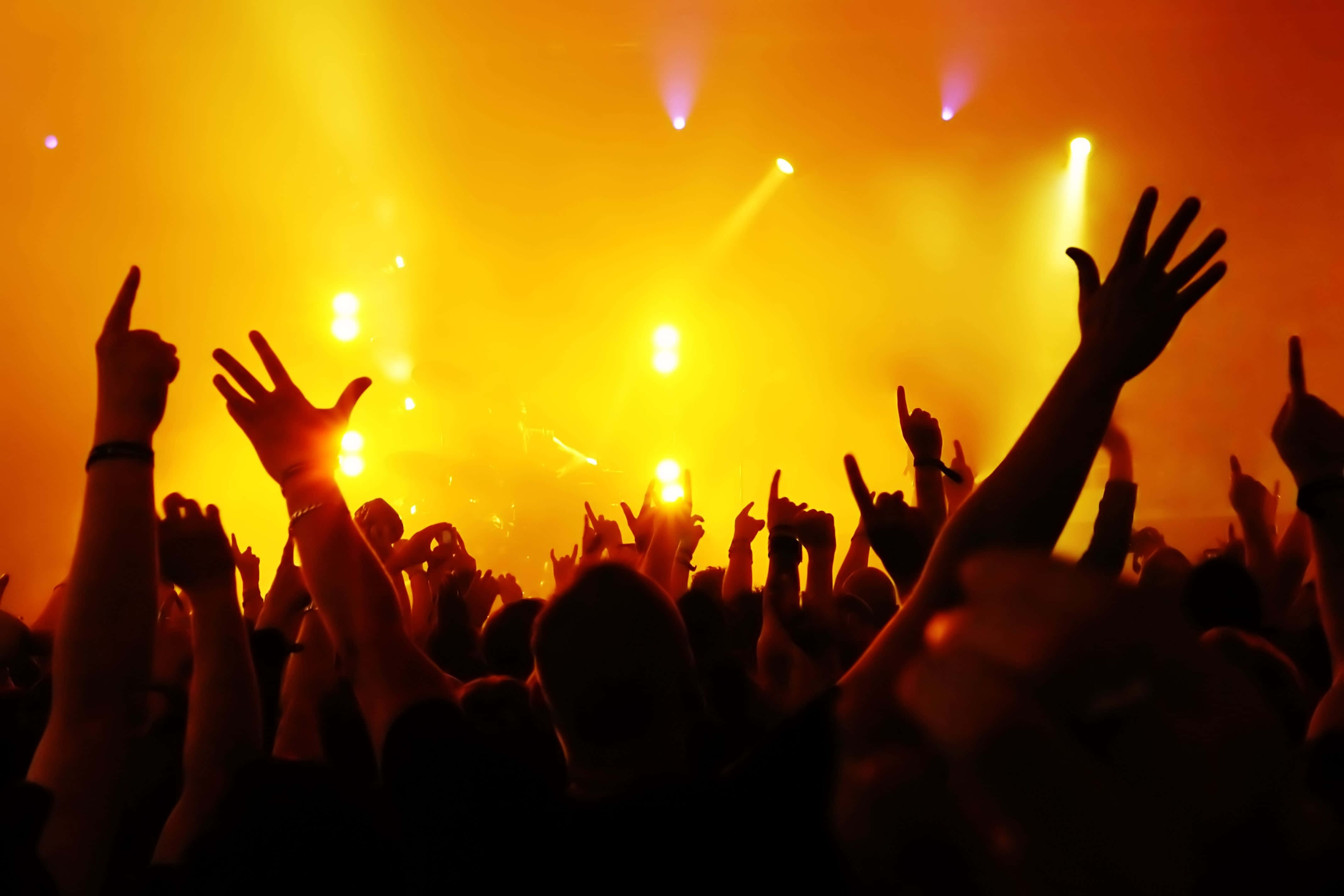 Entertainment 桌布 壁紙 — 剪影的音樂會人群在金色舞台燈光下高舉雙手，充滿活力的慶祝。