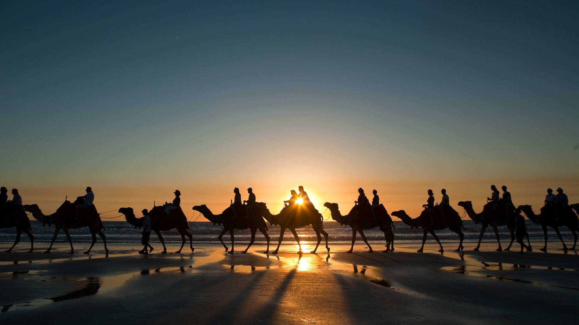 Morocco 桌布 壁紙 — 剪影的駱駝和騎手在濕漉漉的海灘上行進，夕陽在沙灘上投下長長的金色倒影。