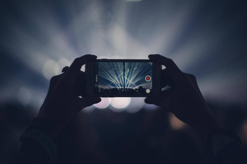 photography iPhone 桌布 壁紙 — 剪影般的手握著手機，錄製從黑暗演唱會場地迸發出的耀眼舞台燈光。
