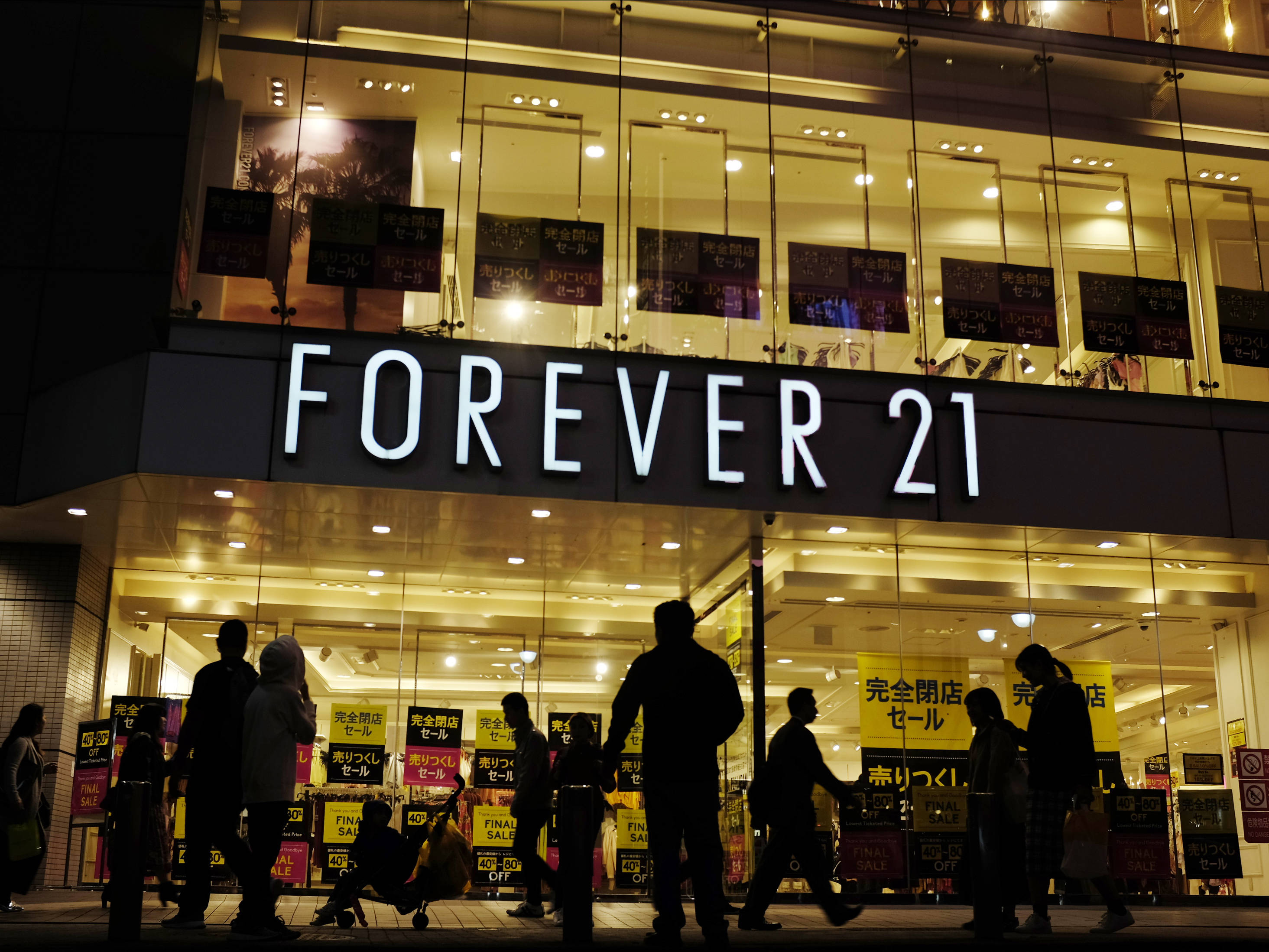 永遠21 桌布 壁紙 — 剪影般的行人夜晚走過一間燈火通明的 Forever 21 商店，玻璃窗內可見日本促銷標誌。