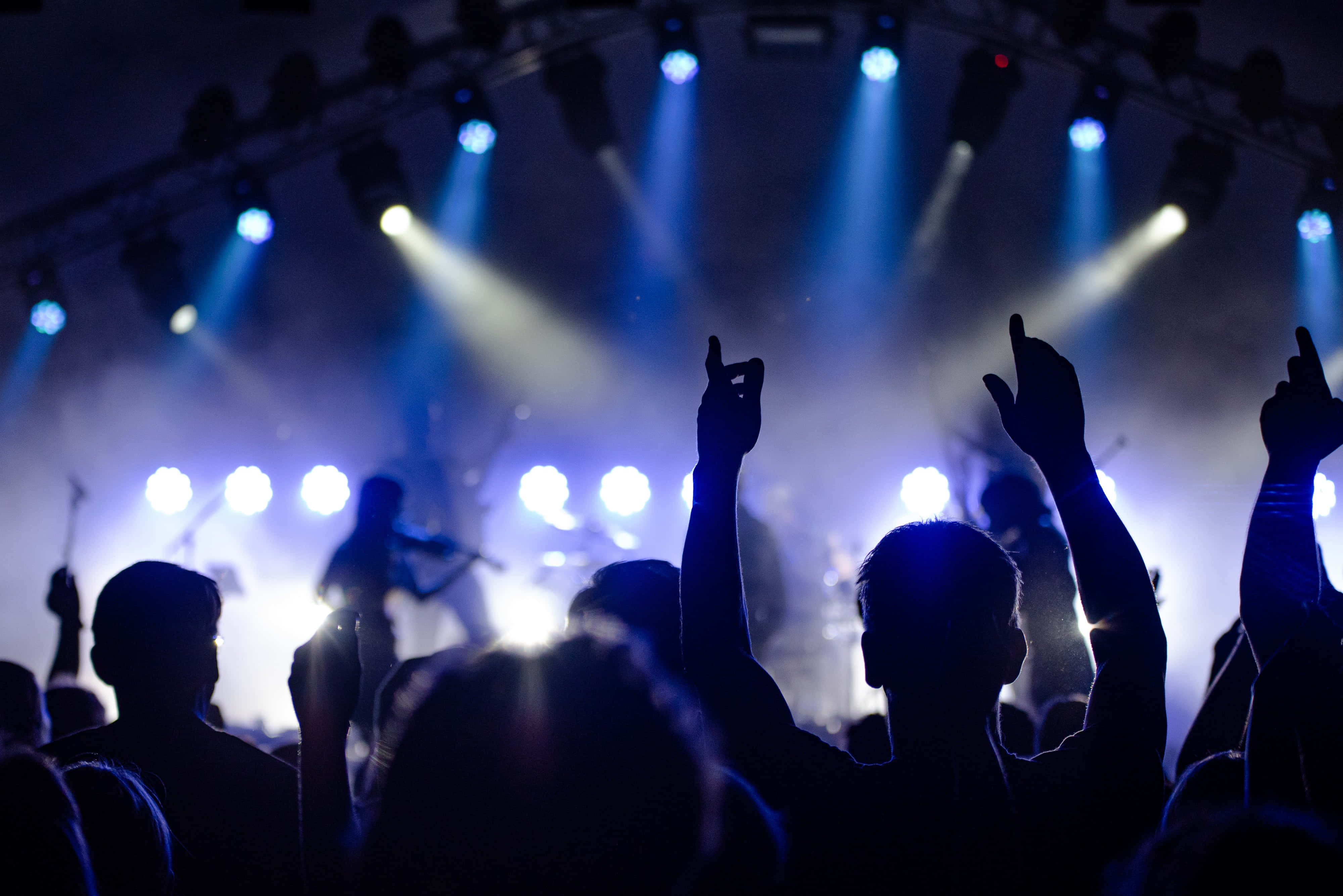 music festival 桌布 壁紙 — 剪影般的音樂會觀眾在充滿活力的藍色舞台燈光下舉起雙手，而音樂家在煙霧瀰漫的舞台上表演。