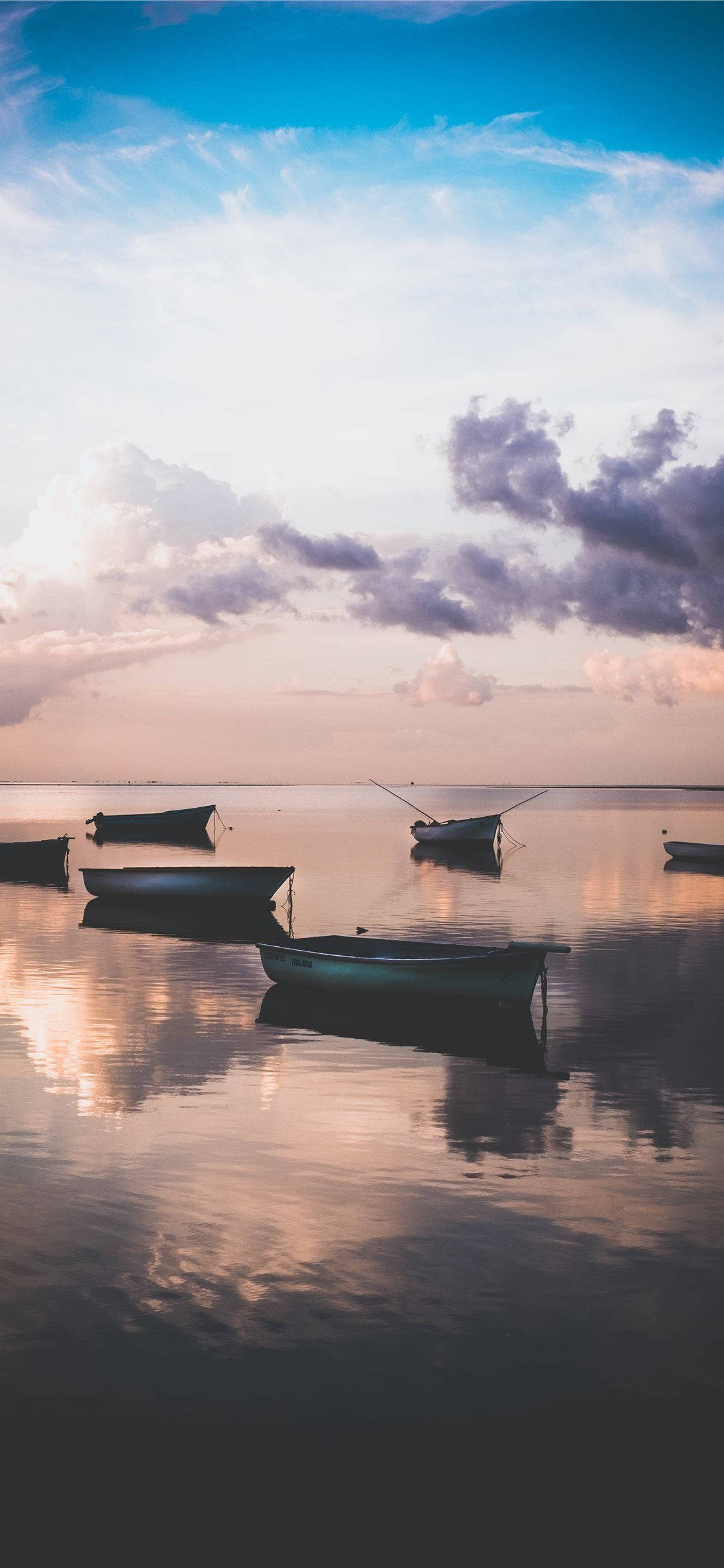 Mauritius 桌布 壁紙 — 剪影船隻平靜地停泊在平靜的水面上，倒映著柔和粉彩的日落天空和縷縷雲彩。