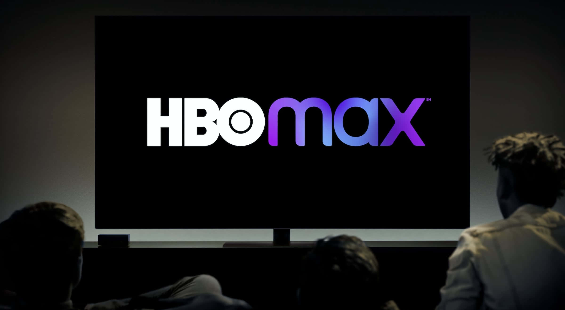 HBO 桌布 壁紙 — 剪影觀眾觀看HBO Max標誌在昏暗的影院中大螢幕上以紫色和白色發光。