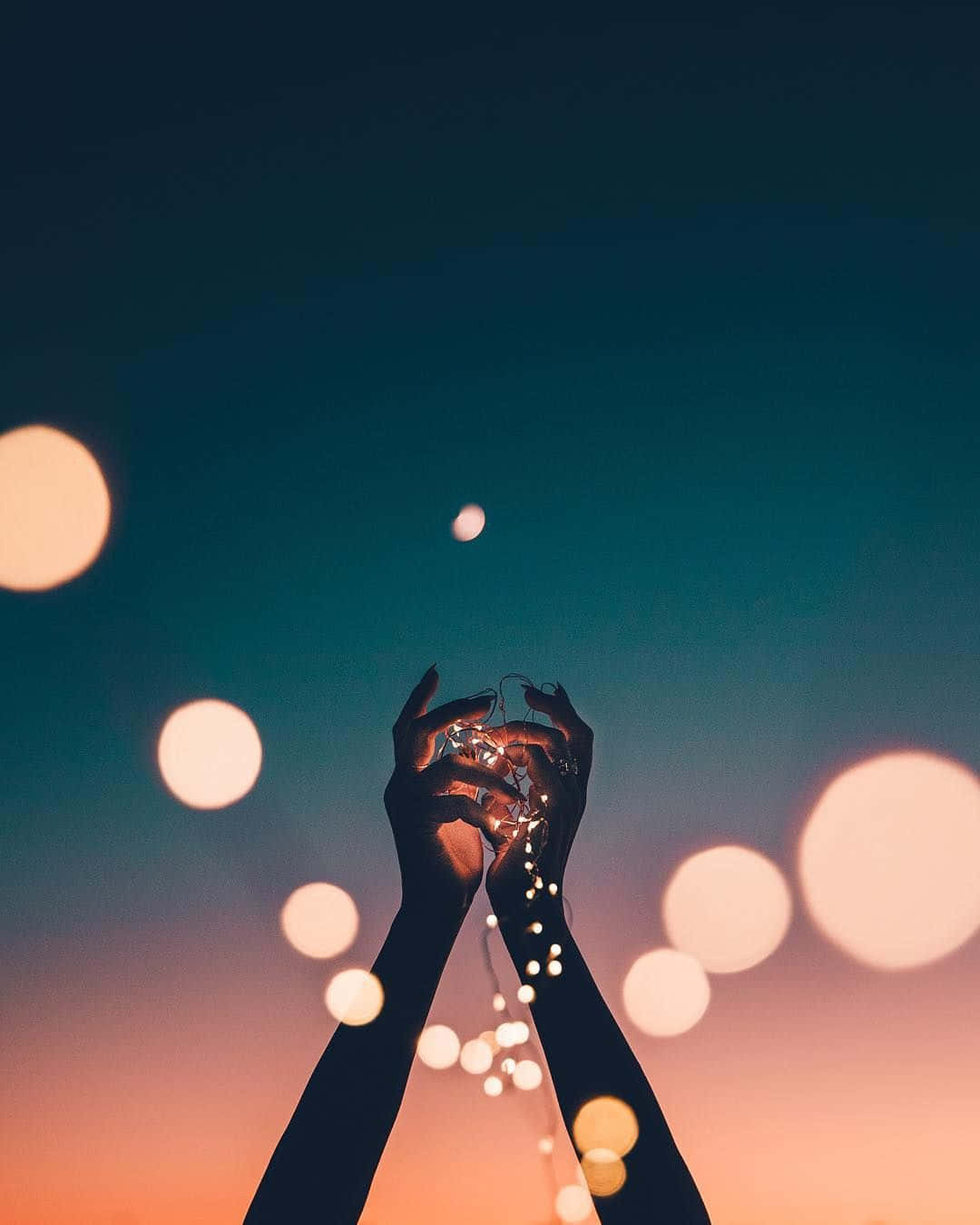 Aesthetic Cute Profile 桌布 壁紙 — 剪影雙手捧著發光的仙女燈，背景是帶有青綠色和蜜桃色散景的暮色天空。