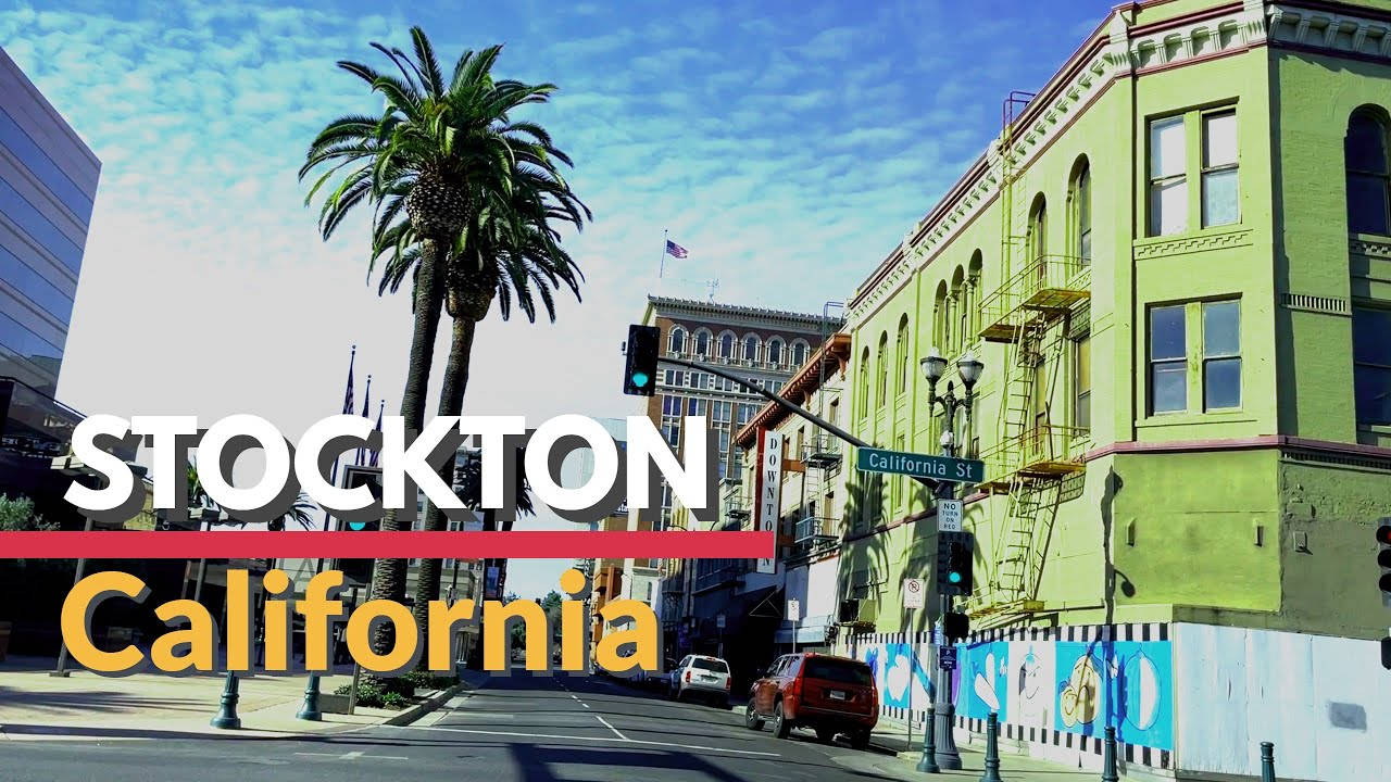California Summer 桌布 壁紙 — 加州斯托克頓充滿活力的街景，高大的棕櫚樹旁有一座亮綠色建築，藍天白雲點綴其間。