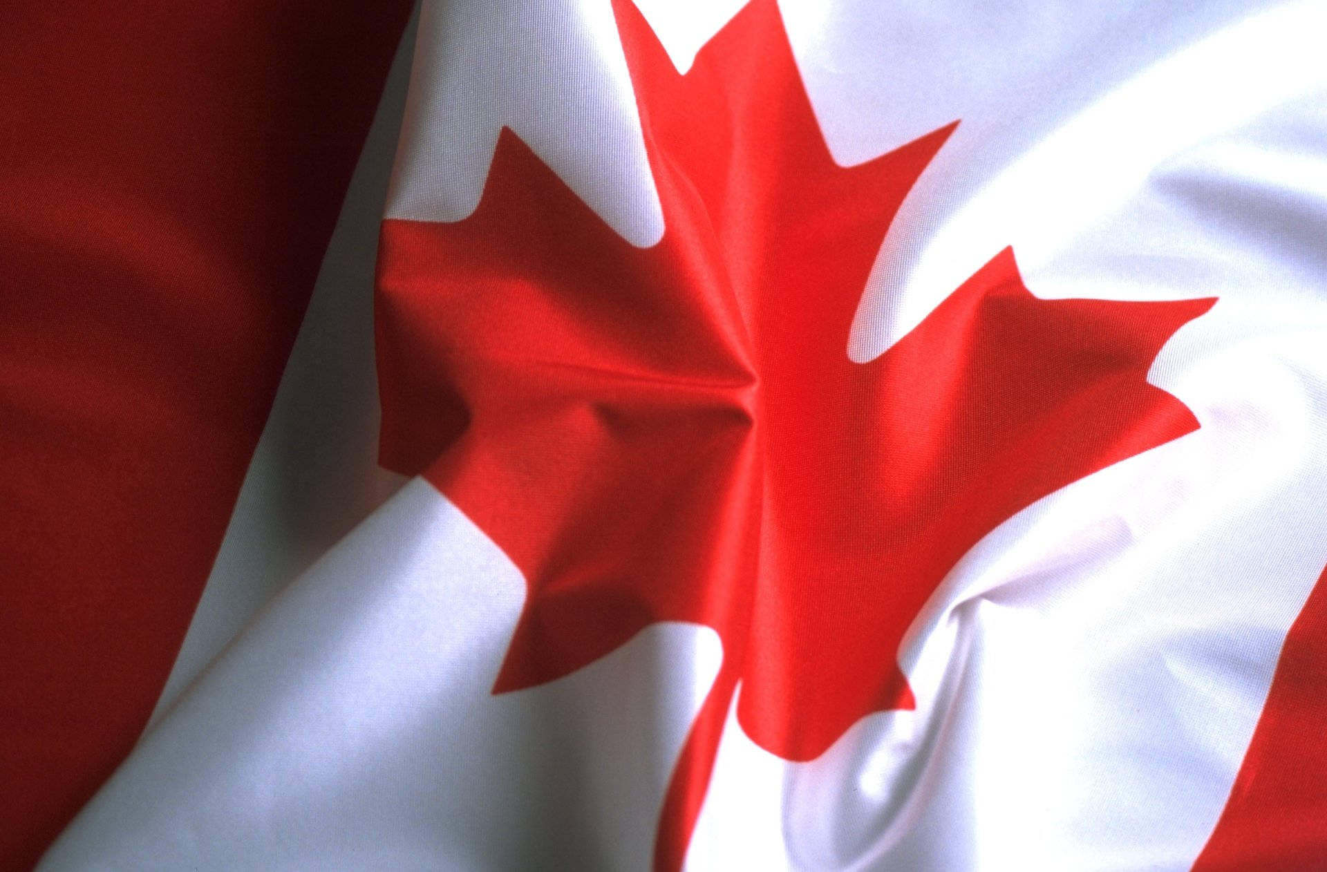 Canada Flag 桌布 壁紙 — 加拿大國旗的特寫，白色布料中央有鮮紅色的楓葉，兩側有紅色垂直條紋，顯示逼真的布料摺痕和高光。