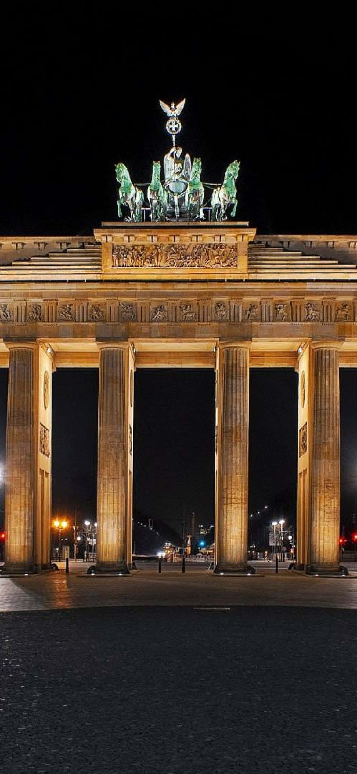 Berlin 桌布 壁紙 — 勃蘭登堡門在夜間被溫暖的燈光照亮，凸顯其新古典主義柱子和四馬戰車雕像，背景是黑暗的天空。