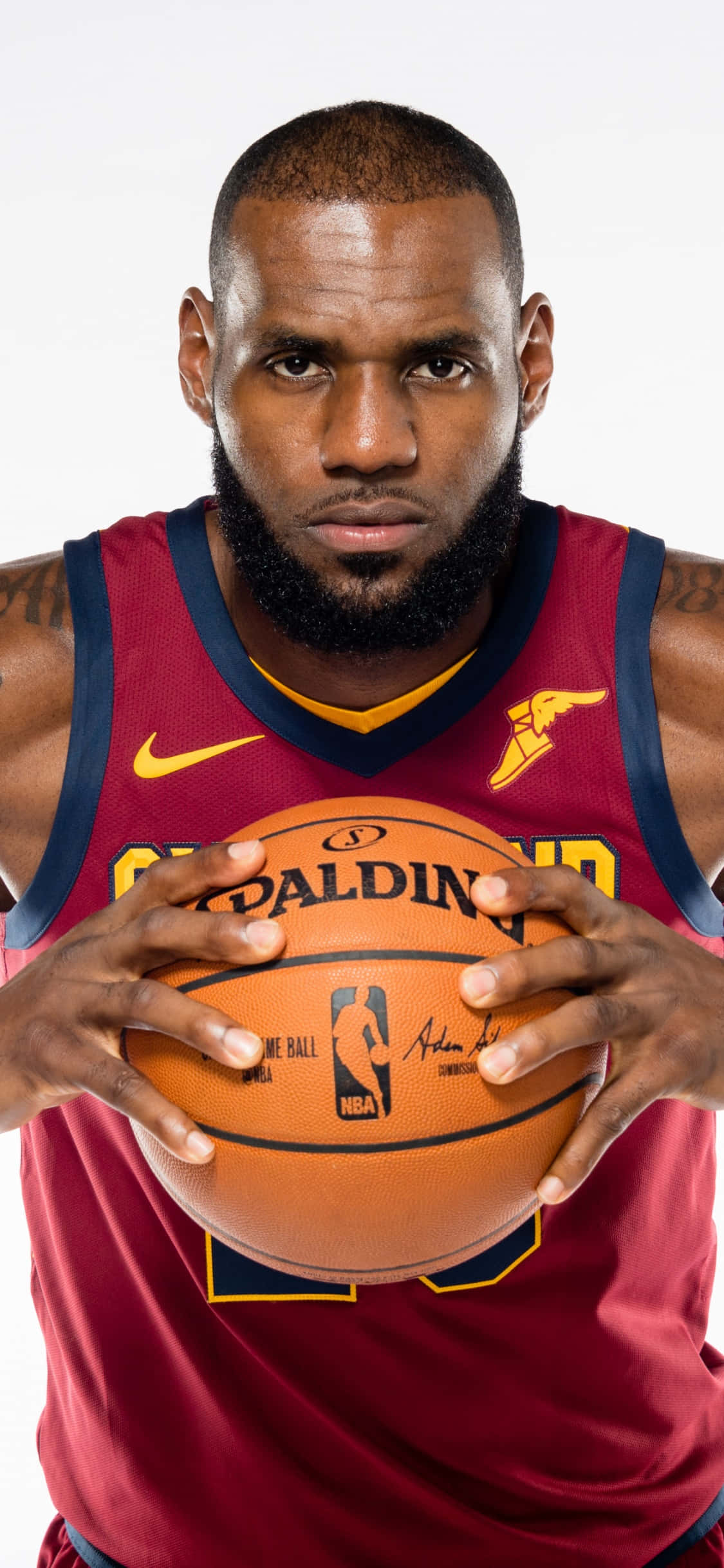 iPhone Xs Basketball 桌布 壁紙 — 勒布朗·詹姆斯身穿栗色克里夫蘭騎士隊球衣，在純白色背景下專注地拿著一個Spalding籃球。