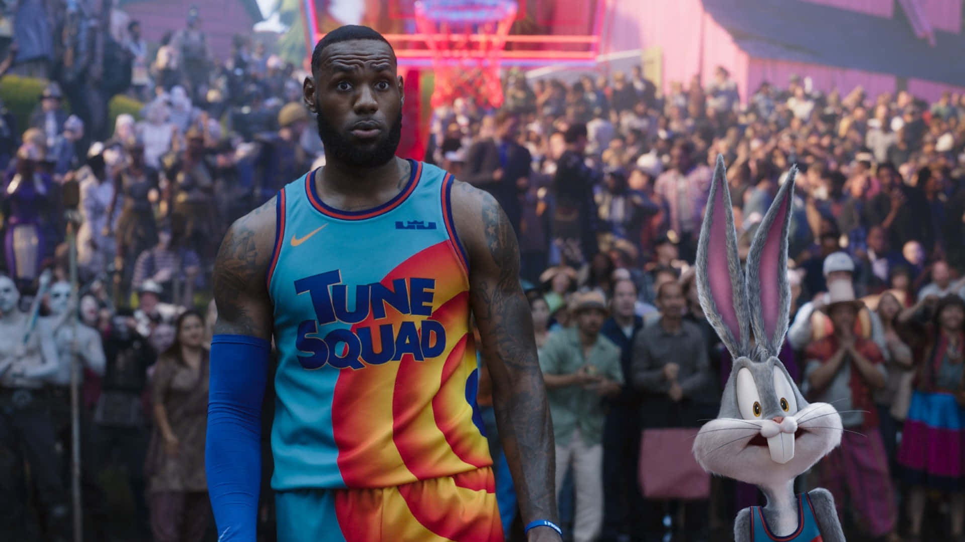 勒布朗·詹姆斯 桌布 壁紙 — 勒布朗·詹姆斯身穿色彩繽紛的Tune Squad球衣，在明亮的燈光下站在擠滿觀眾的場館內，旁邊是賓尼兔。