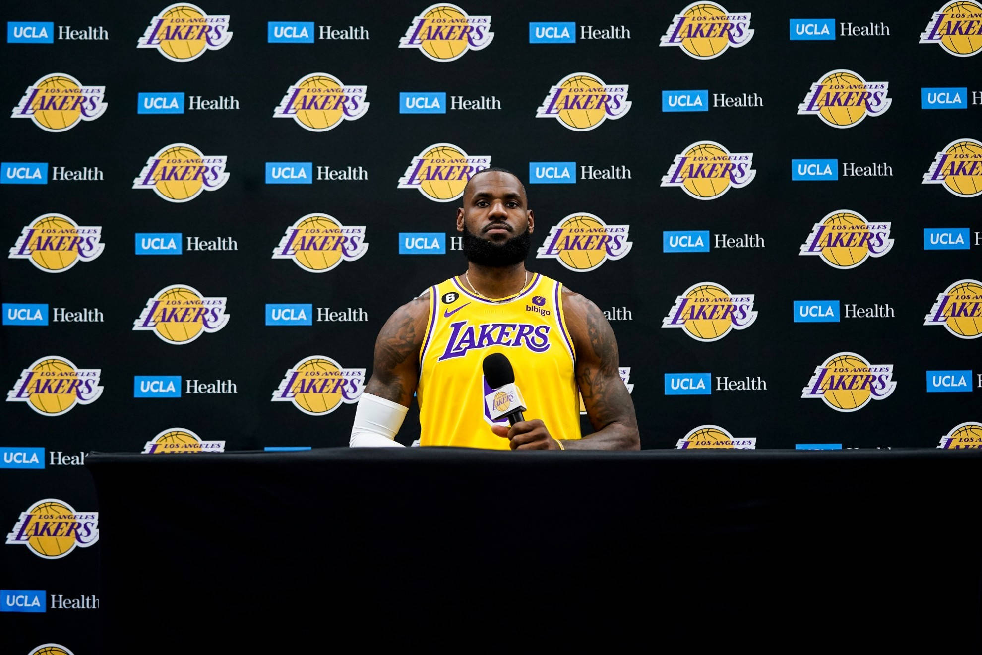 NBA 桌布 壁紙 — 勒布朗·詹姆斯身穿黃色湖人球衣，在品牌背景的新聞發布會上對著麥克風發言。