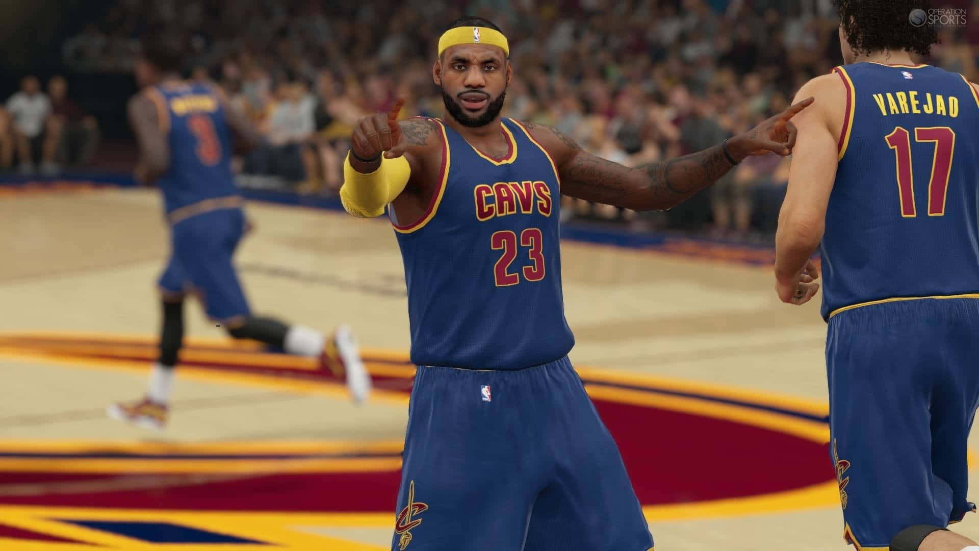 NBA 2k 桌布 壁紙 — 勒布朗詹姆斯身穿藍色騎士隊球衣，在充滿活力的球場上與隊友進行籃球比賽時自信地指向對方。