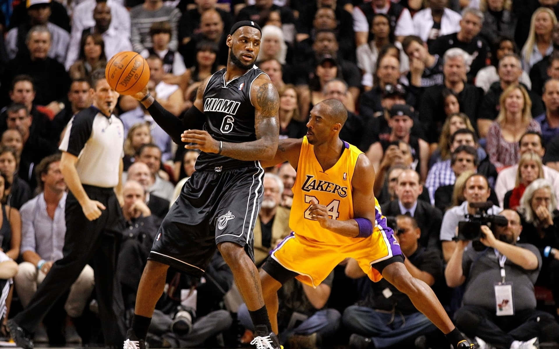 NBA 桌布 壁紙 — 勒布朗詹姆斯身穿邁阿密熱火球衣運球，同時被身穿湖人球衣的柯比布萊恩緊密防守，在一場座無虛席的籃球比賽中。
