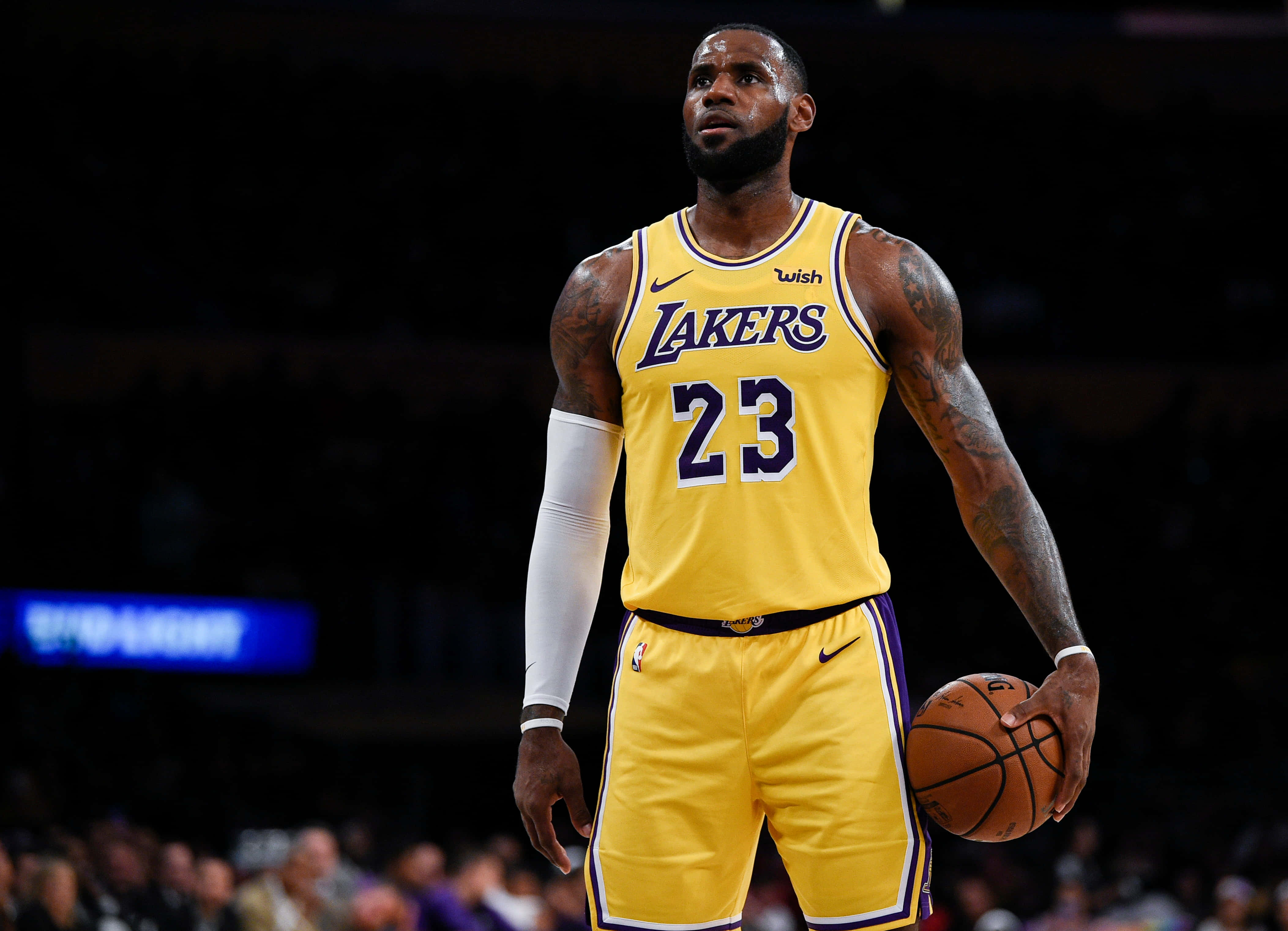 NBA 桌布 壁紙 — 勒布朗詹姆斯身穿黃色湖人球衣，在燈光昏暗的球場上手持籃球，背景有模糊的觀眾。