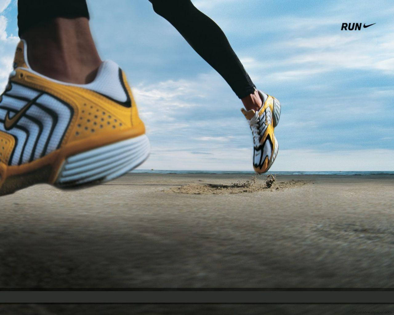 Marathon 桌布 壁紙 — 動態低角度拍攝跑者黃白色Nike鞋在沙灘上邁步，天空多雲。