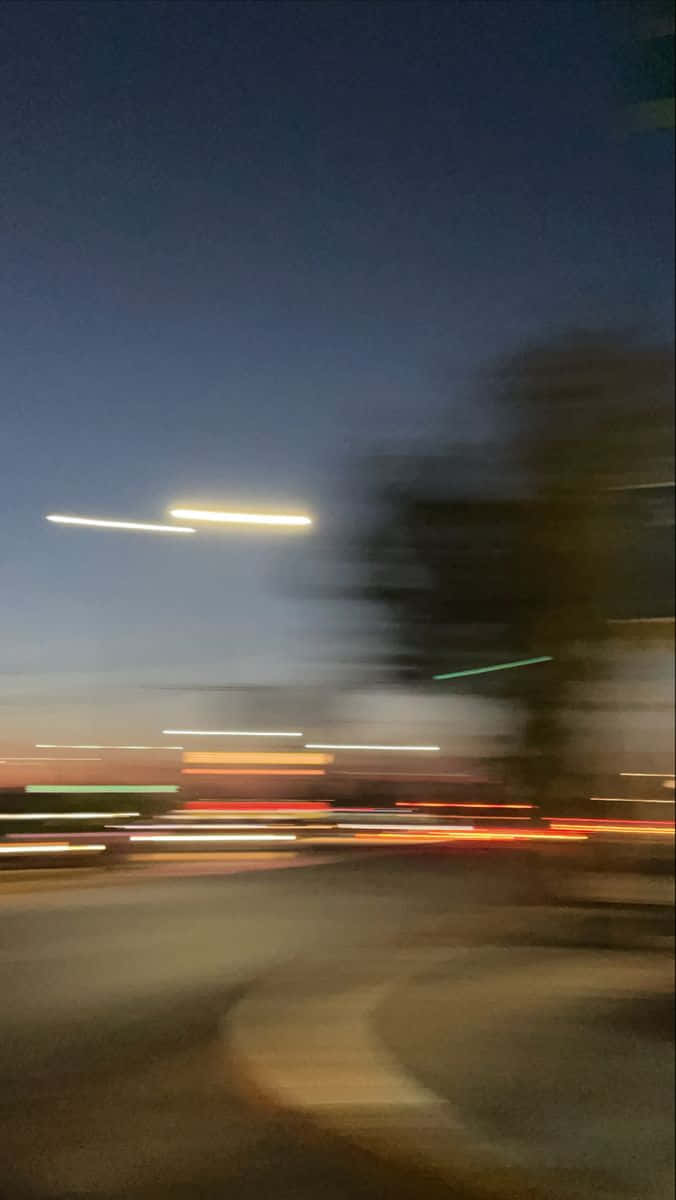 日落 桌布 壁紙 — 動態模糊的夜景，車燈在深藍色天空和模糊的路邊樹木間劃出光痕。