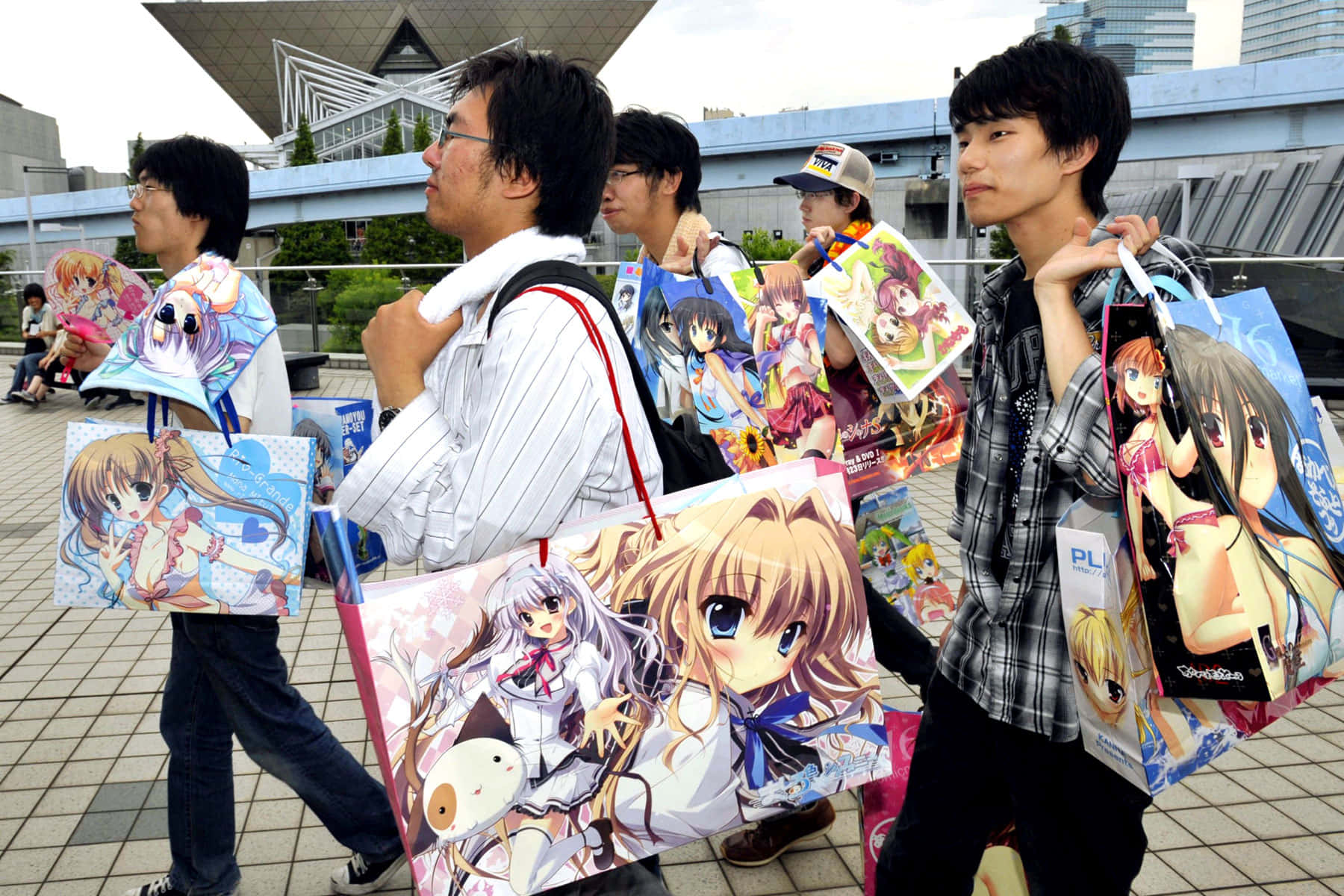 Otaku Culture 桌布 壁紙 — 動漫迷在戶外行走，帶著印有動漫女孩角色的彩色袋子參加會議。