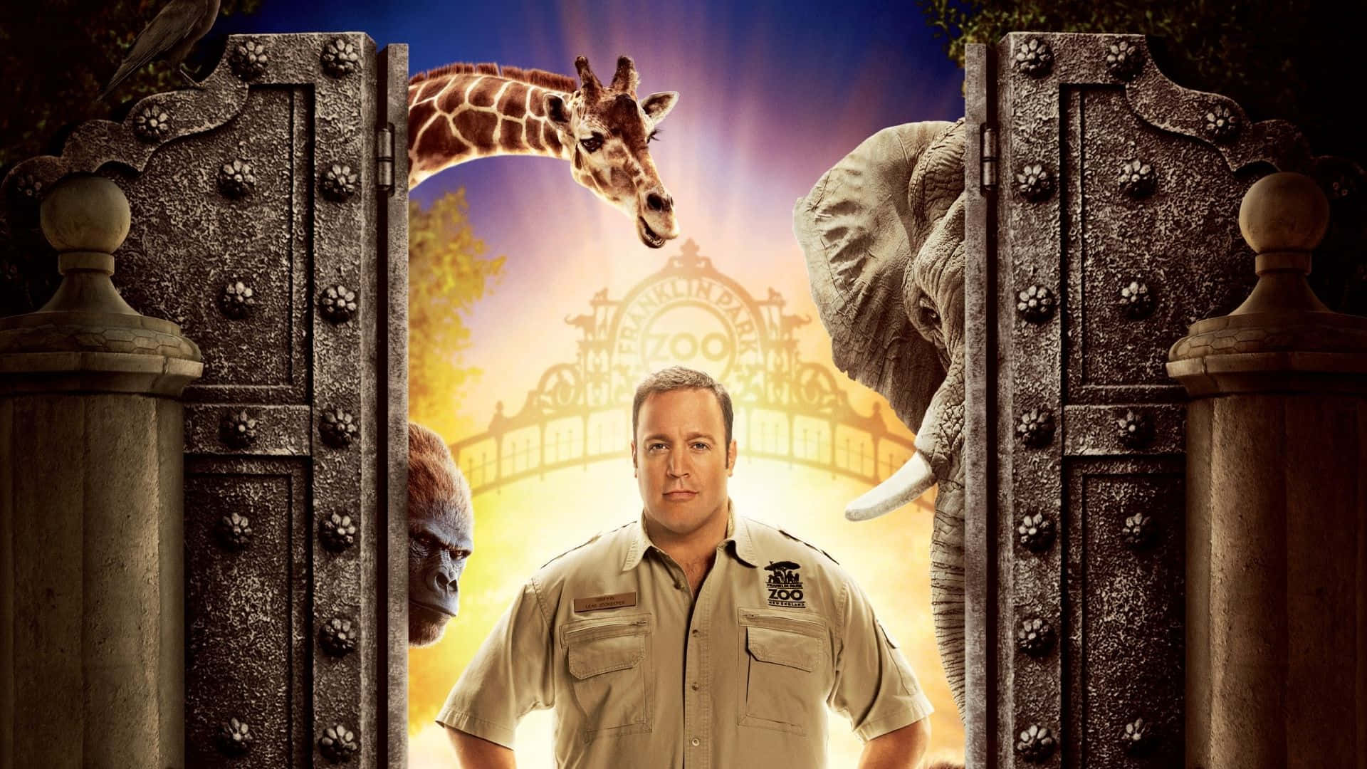 Kevin James 桌布 壁紙 — 動物園管理員站在華麗的大門前，長頸鹿、大象和大猩猩從門後探出頭來，背景是閃耀的日落。