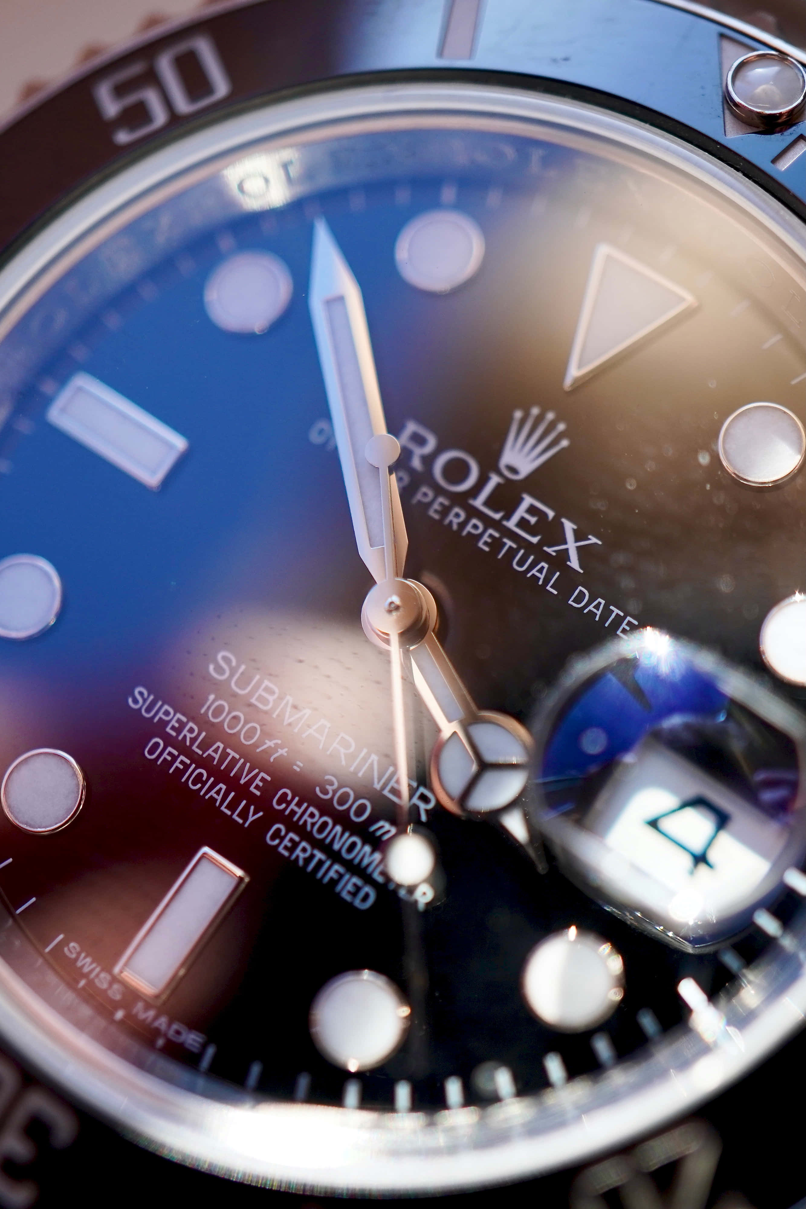 Rolex 桌布 壁紙 — 勞力士潛航者型手錶錶盤特寫，配備藍色漸變錶盤和夜光時標，在溫暖燈光下拍攝。