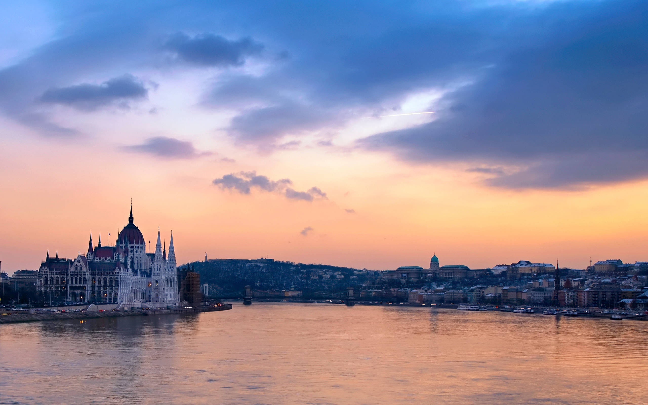 Hungary 桌布 壁紙 — 匈牙利國會大廈在多瑙河上夕陽下閃耀金光，上方有戲劇性的紫色和橙色雲彩。