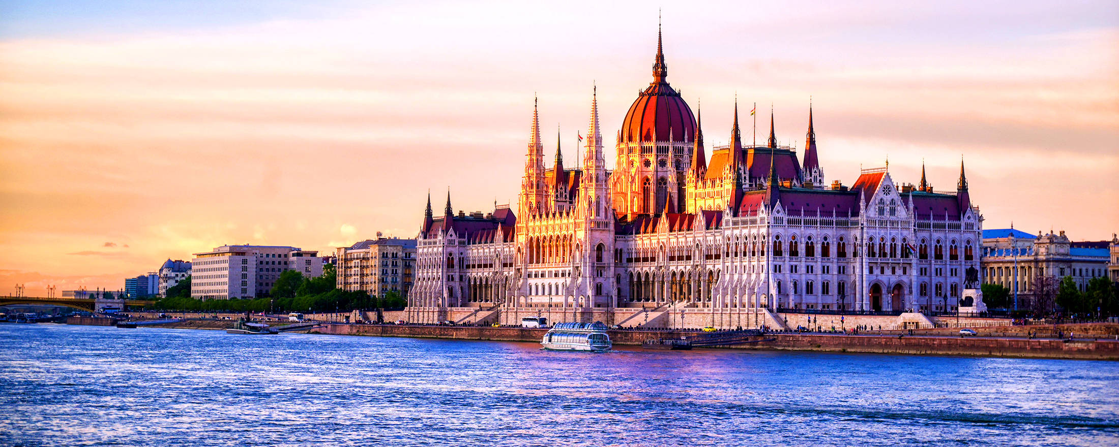 budapest 桌布 壁紙 — 匈牙利國會大廈在日落時閃耀金光，倒映在多瑙河中，一艘小船駛過。