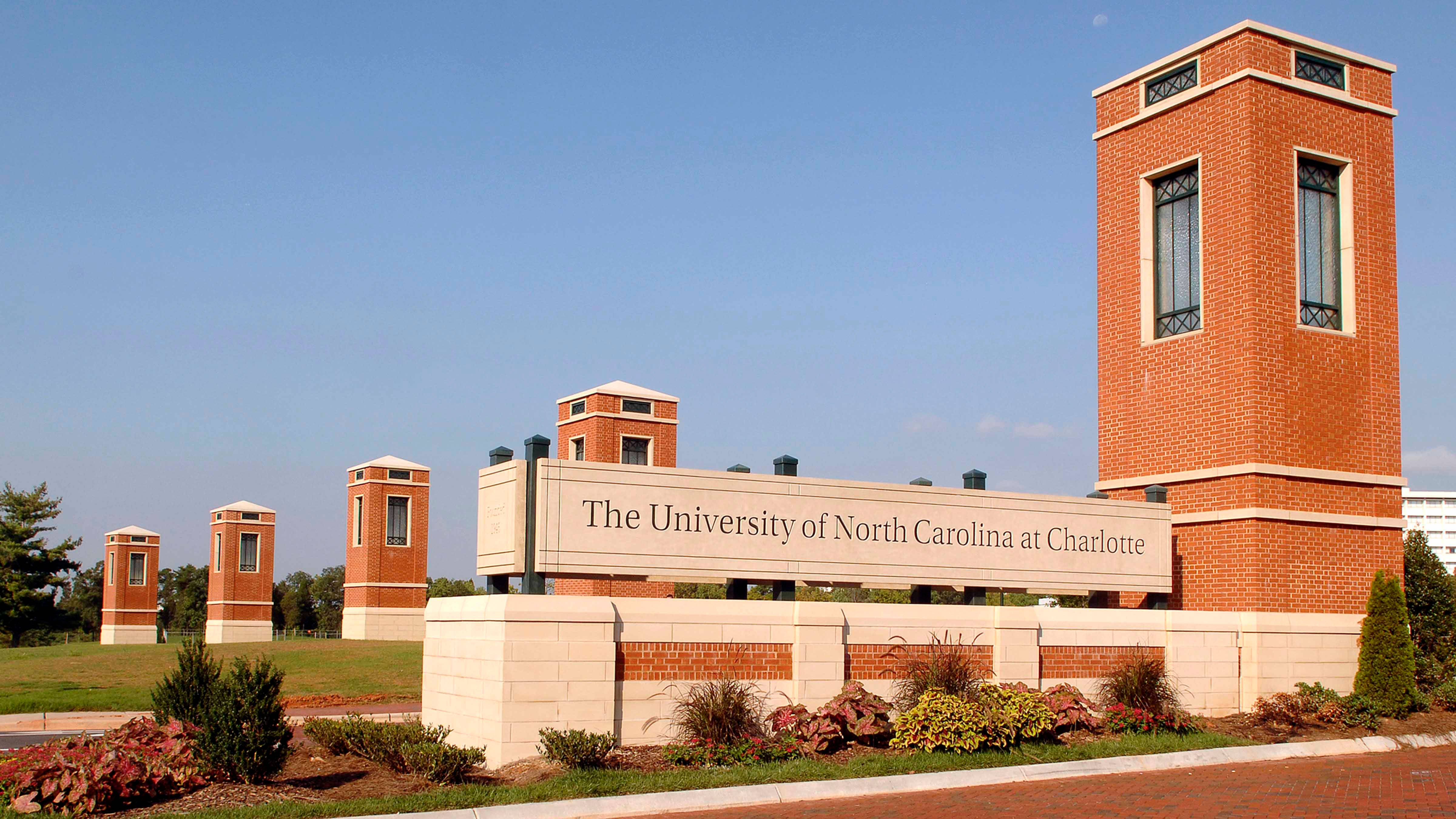 North Carolina 桌布 壁紙 — 北卡羅來納大學夏洛特分校的一個宏偉磚砌入口標誌，矗立在晴朗的藍天下，周圍是修剪整齊的園林景觀。