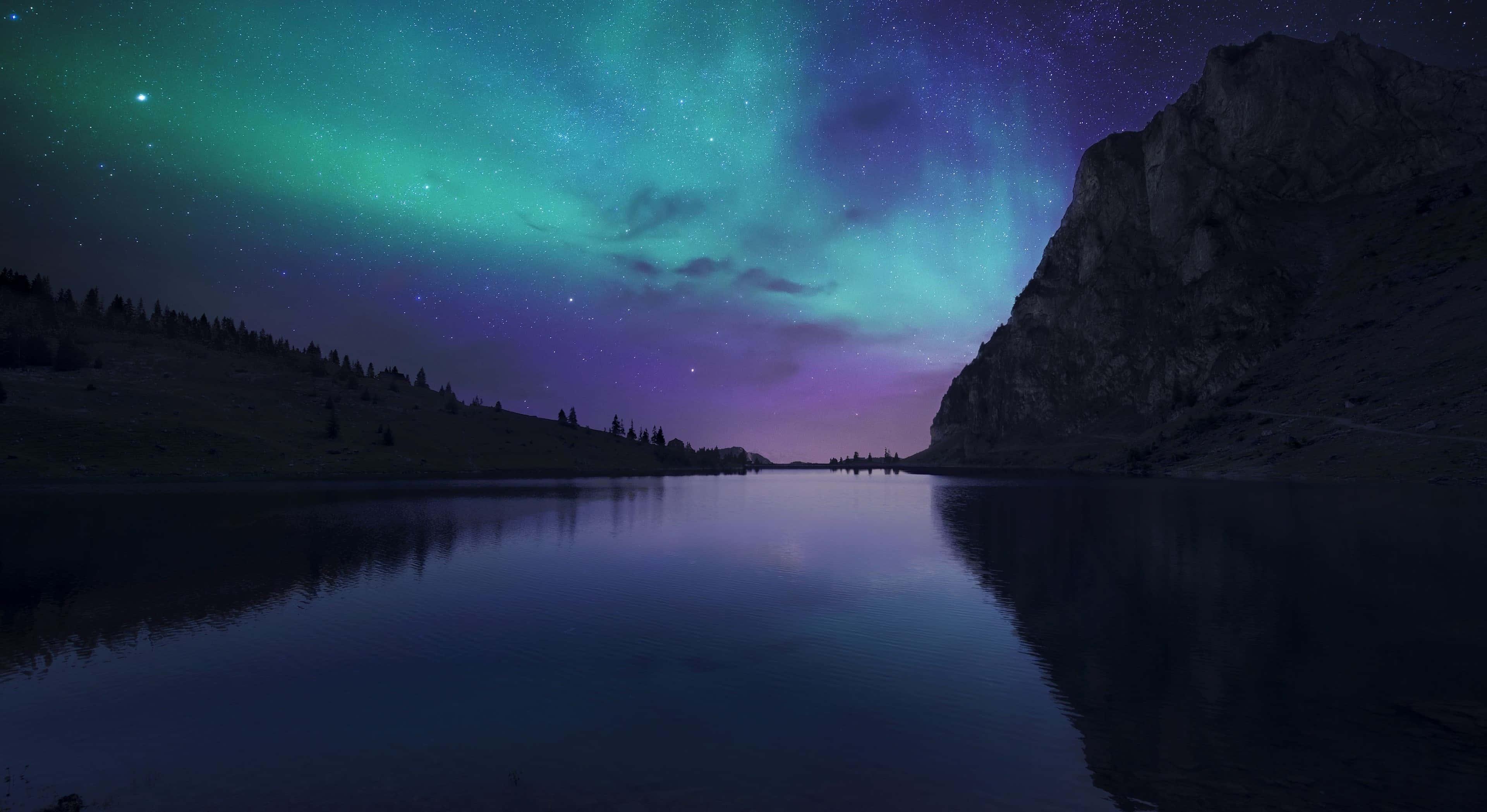Aurora 桌布 壁紙 — 北極光在充滿活力的綠色和紫色中舞動，越過黑暗山脈環繞的平靜湖泊上方的星空夜空。