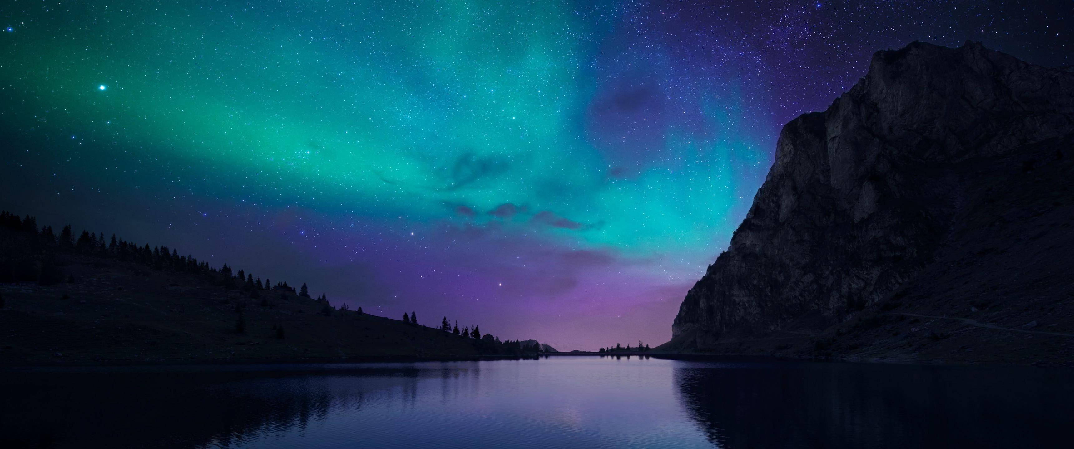 aurora borealis 桌布 壁紙 — 北極光在平靜的湖泊和黑暗的山脈剪影上方的星空夜空中以鮮豔的綠色和紫色舞動。