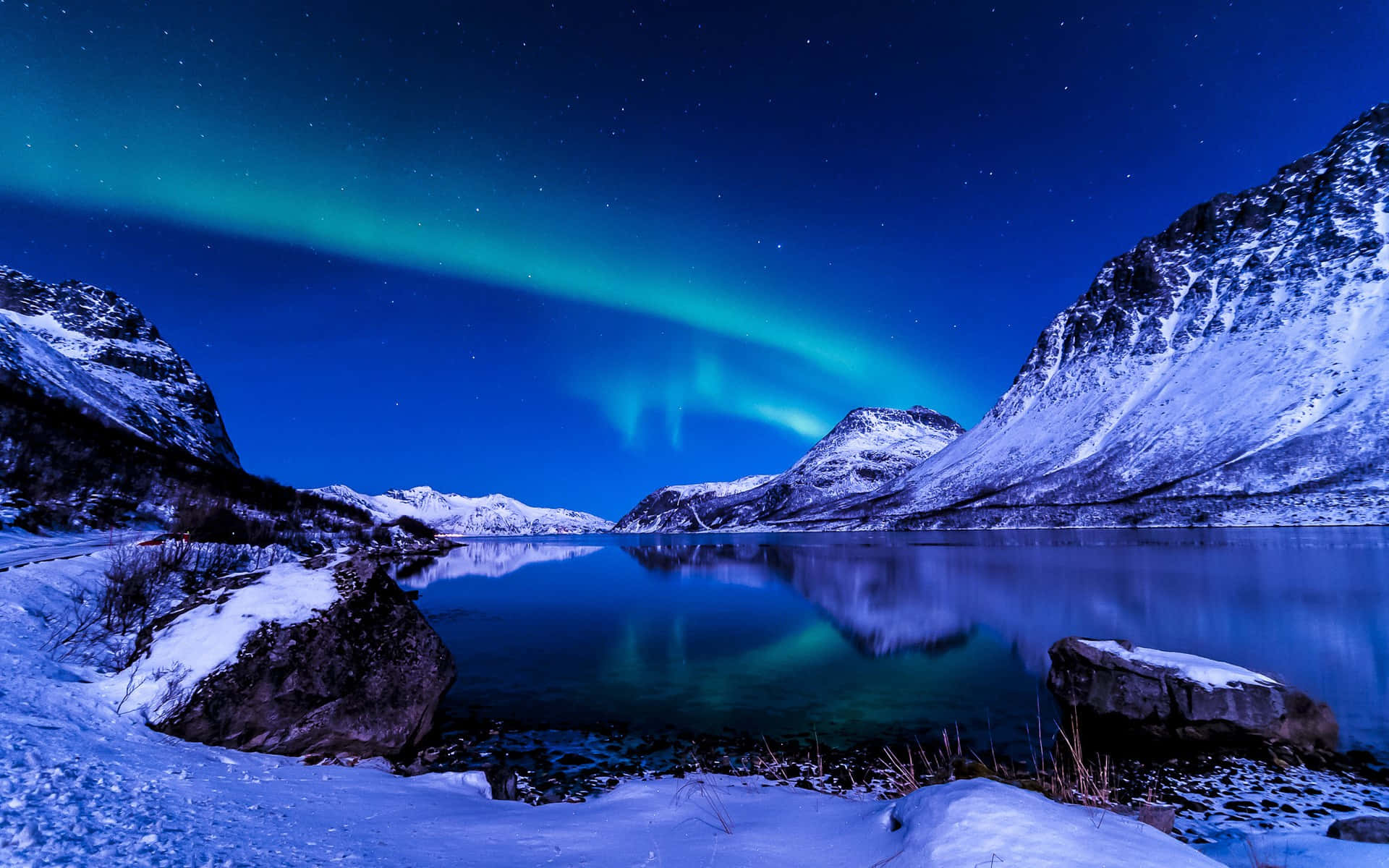 極光 桌布 壁紙 — 北極光在繁星點點的夜空上，以鮮豔的綠色舞動，下方是白雪覆蓋的山間湖泊。