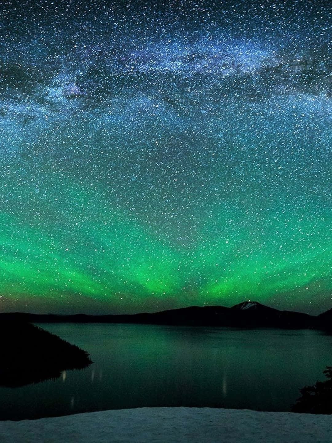 自然 桌布 壁紙 — 北極光在繁星點點的夜空上舞動著鮮豔的綠色，下方是平靜的湖泊，湖岸覆蓋著薄雪。