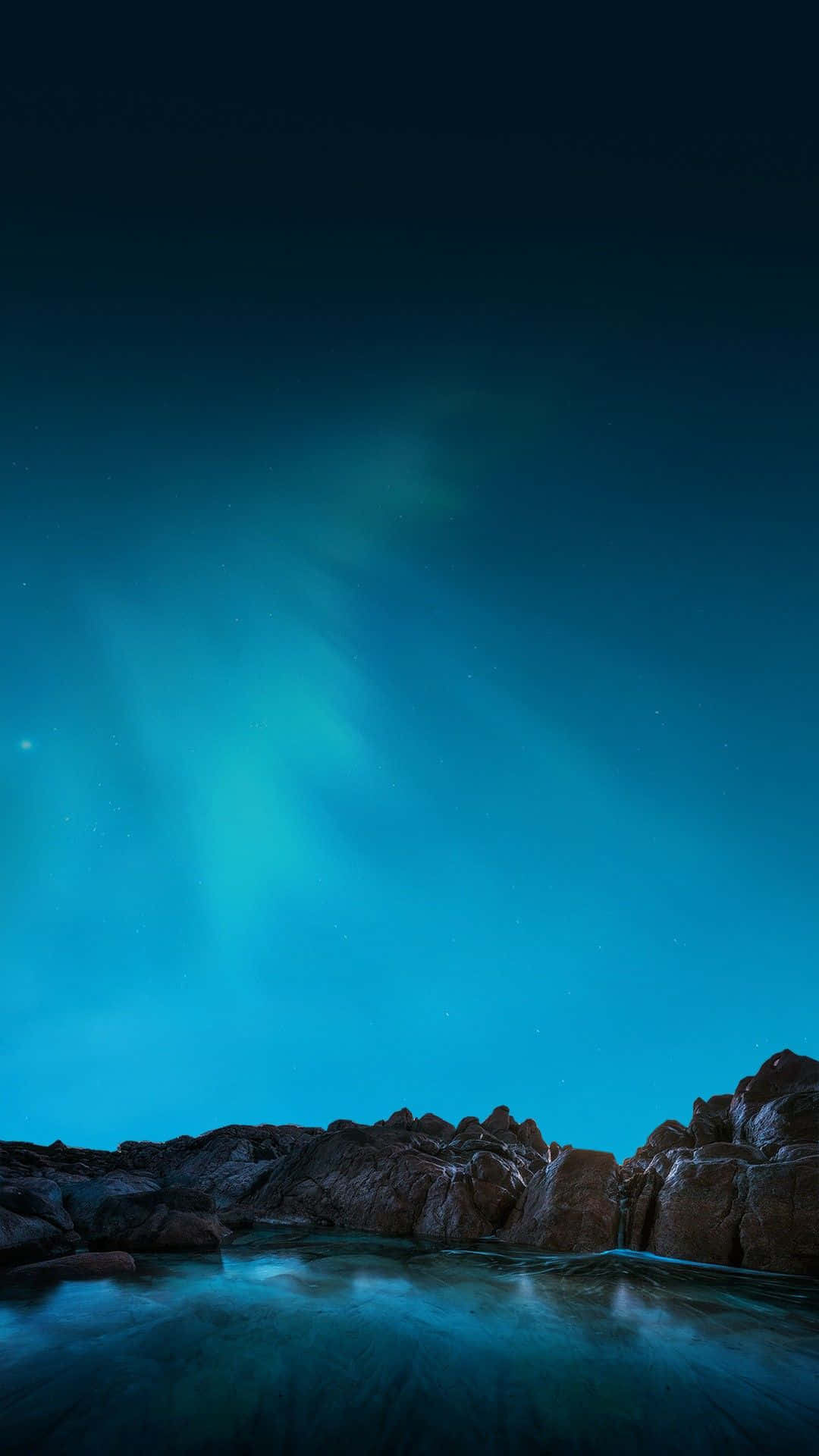 藍色美學 桌布 壁紙 — 北極光在繁星點點的夜空中，以鮮豔的青綠色在黑暗的岩石海岸和寧靜的水面上舞動。