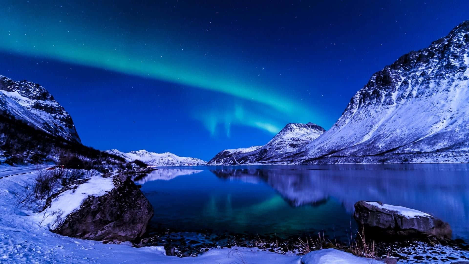 Chill Aesthetic 桌布 壁紙 — 北極光在繁星點點的夜空中以鮮豔的綠色舞動，映照在白雪覆蓋的山間湖面上。