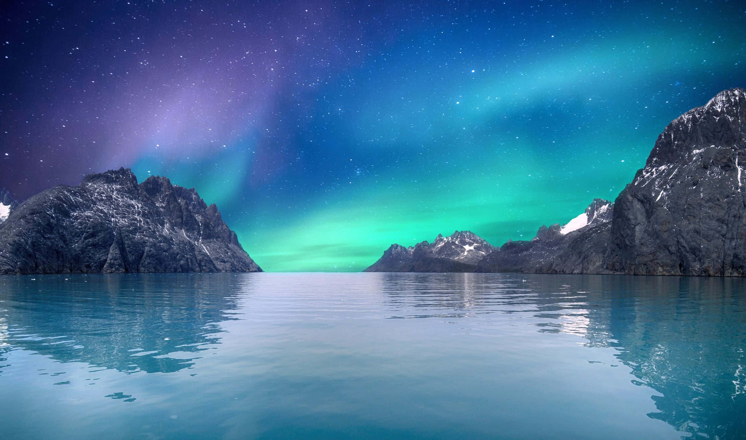2440x1440 Desktop Pc 桌布 壁紙 — 北極光在繁星點點的夜空中以鮮豔的綠色和紫色舞動，映照在平靜的藍綠色水面上，上方是積雪的山峰。