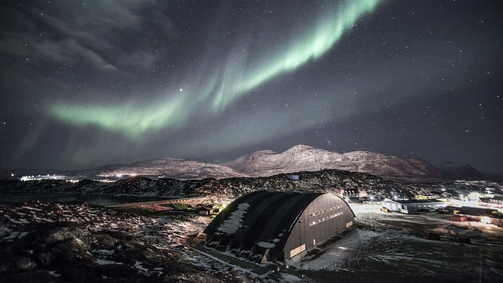 Greenland 桌布 壁紙 — 北極光在繁星點點的夜空中舞動，照耀著群山環抱中積雪的北極研究站。
