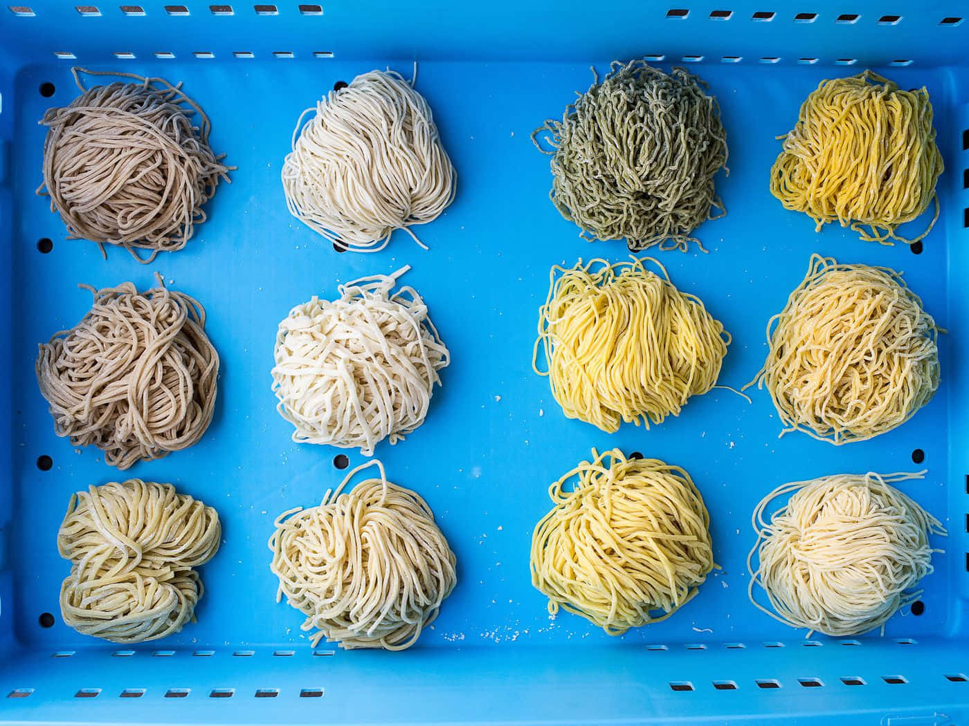 Noodles 桌布 壁紙 — 十二束色彩繽紛的麵條，以大地色和黃色調整齊排列在亮藍色塑膠托盤中。