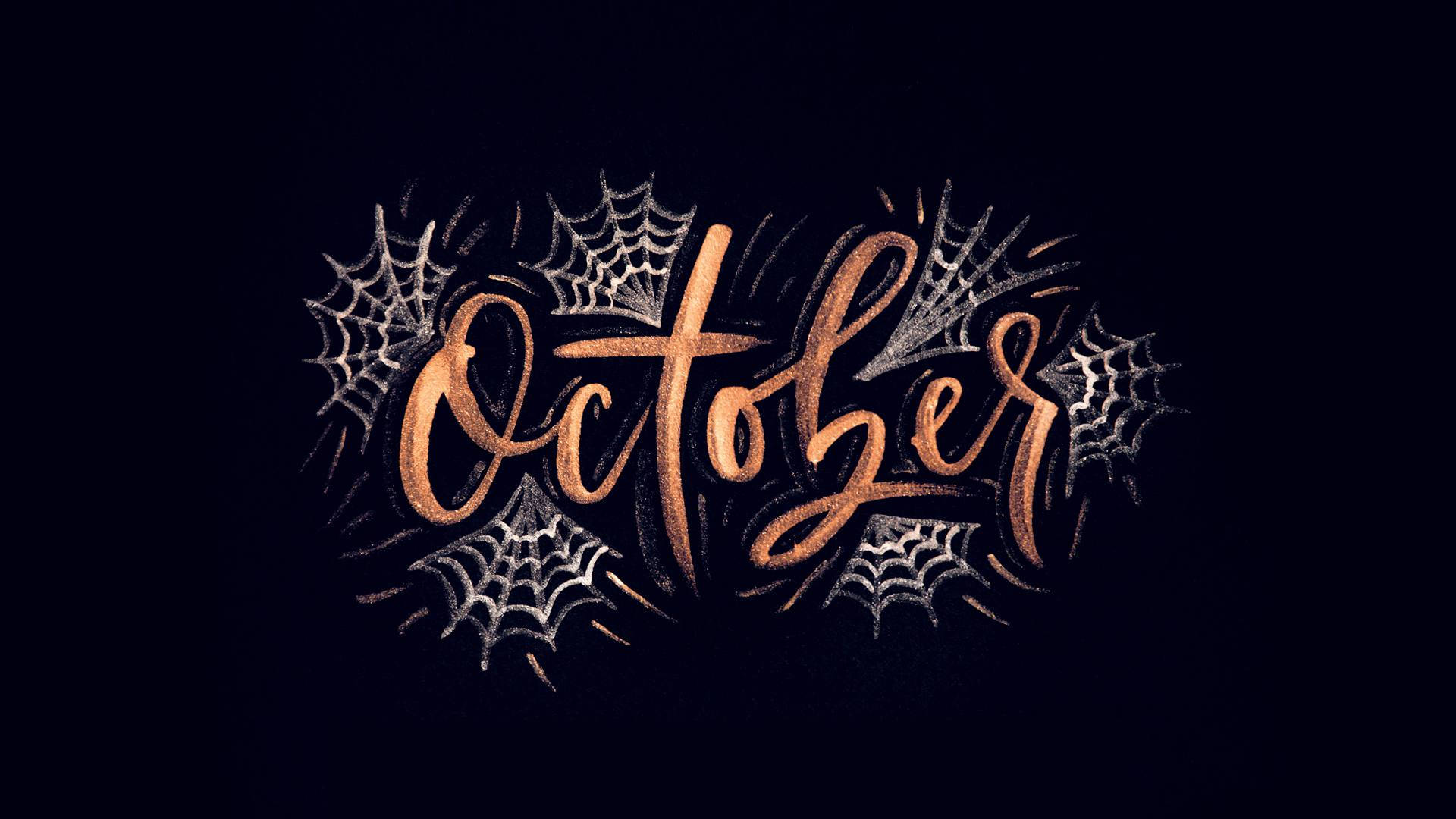 Cute Aesthetic Halloween 桌布 壁紙 — 「十月」這個詞以優雅的古銅色字體書寫，周圍環繞著精緻的銀色蜘蛛網，背景為深色。