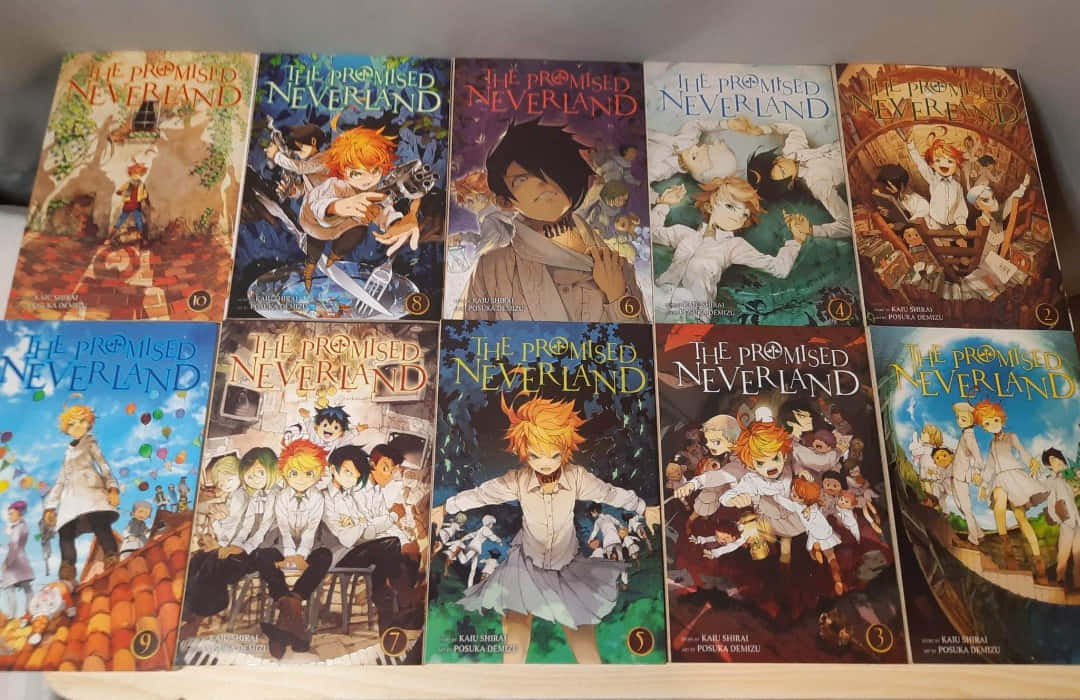 動漫 桌布 壁紙 — 十本色彩繽紛的《約定的夢幻島》漫畫整齊排列在書架上，展示充滿活力的封面藝術，帶有動漫角色。